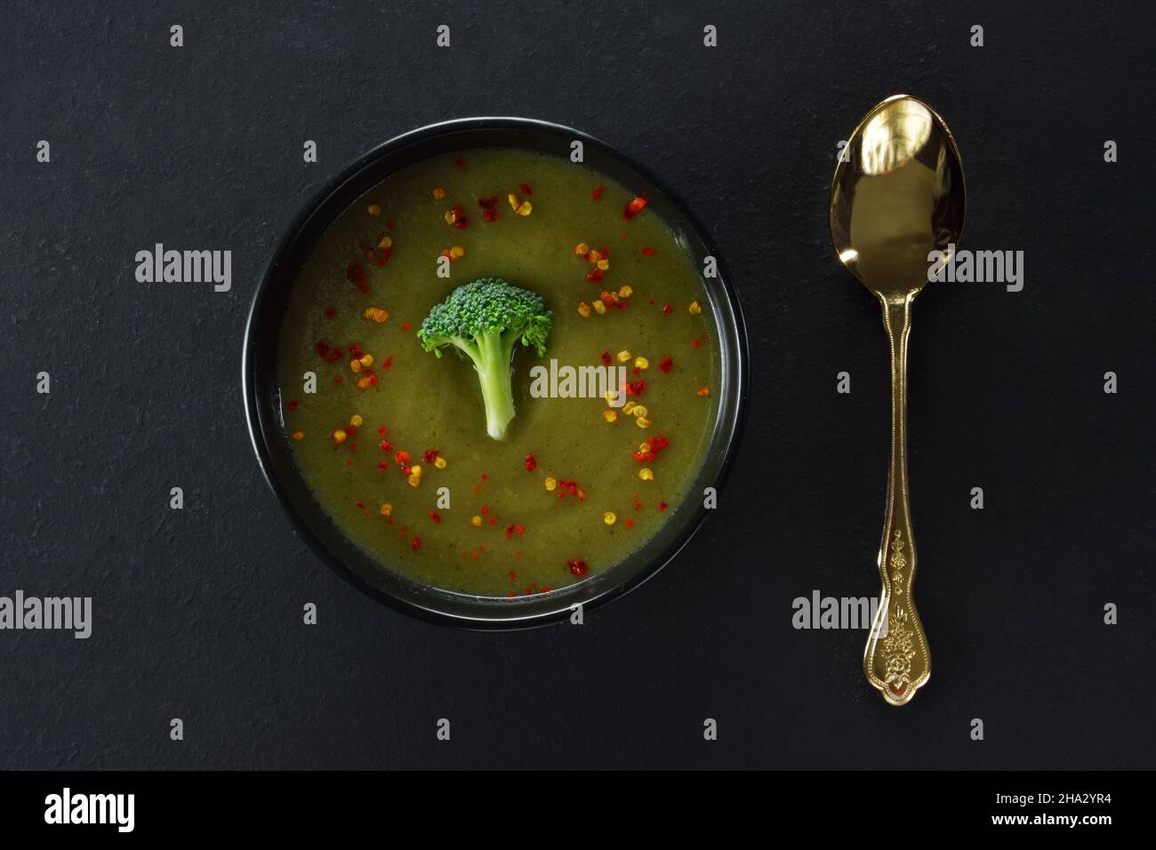 Soupe de brocoli sur un bol et cuillère dorée sur une table noire Banque D'Images