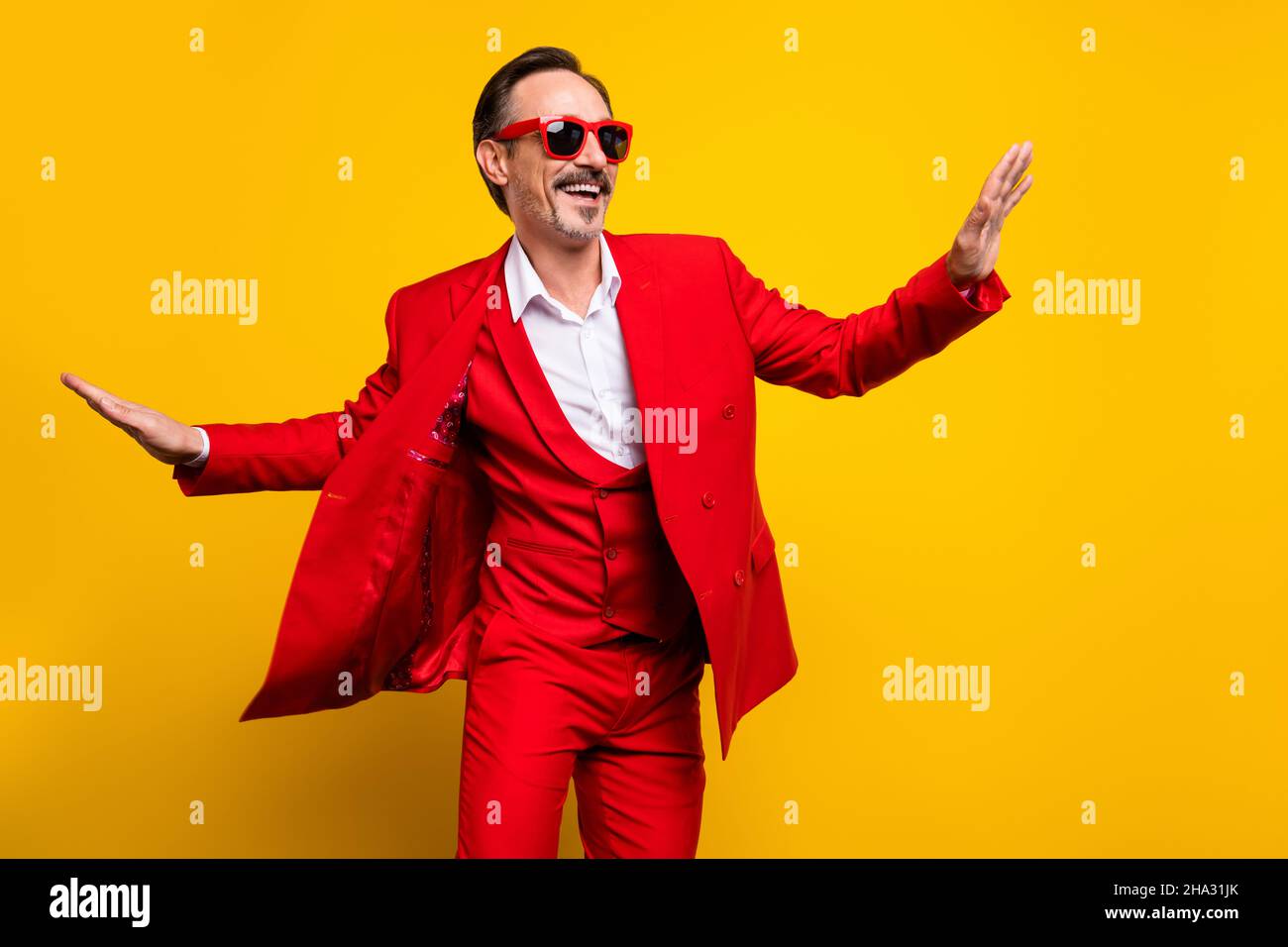 Photo de bonne humeur funky homme d'âge moyen dansant en rouge tuxedo lunettes de soleil sentiment jeune isolé sur fond jaune Banque D'Images