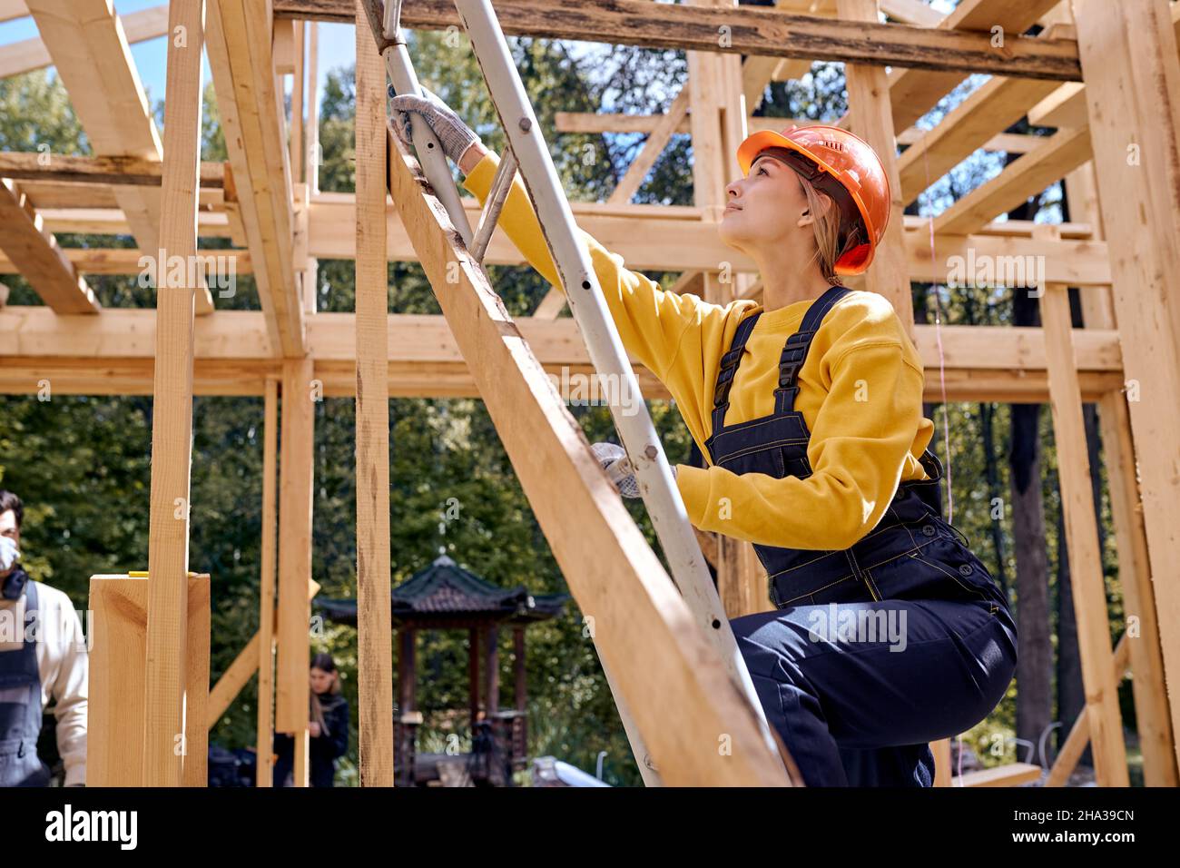 Idées de rénovation et d'extension de maisons en bois.Femme sur l'échelle, monte sur le toit.Femme caucasienne travaillant dur dans l'uniforme de travail et la sécurité dur Banque D'Images