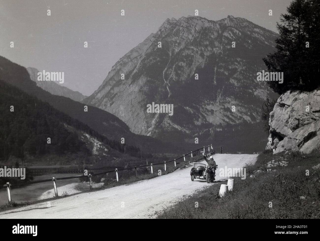 1930s, historique, sur une route de montagne poussiéreuse, une dame assise sur une voiture scoute indienne avec un side-car, en signe de route à la personne au loin prenant sa photo, Alpes, France. Banque D'Images