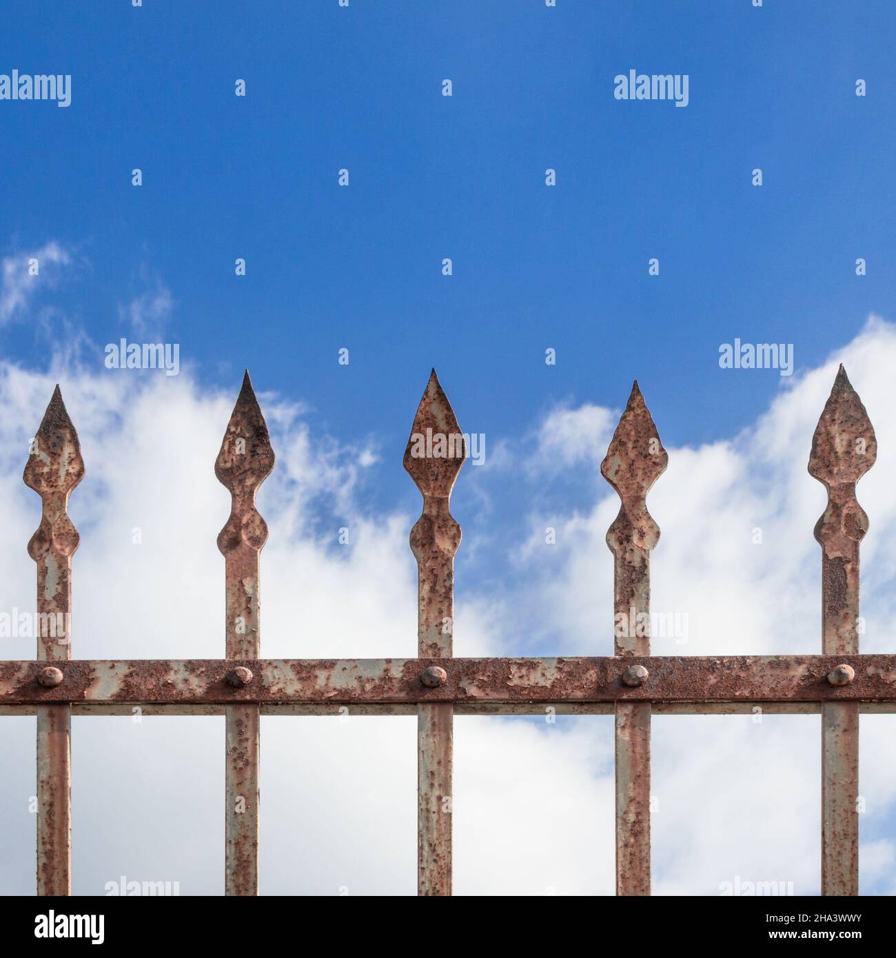 Détails d'une clôture rouillée décorée de têtes de fer et de ciel et de nuages en arrière-plan. Banque D'Images