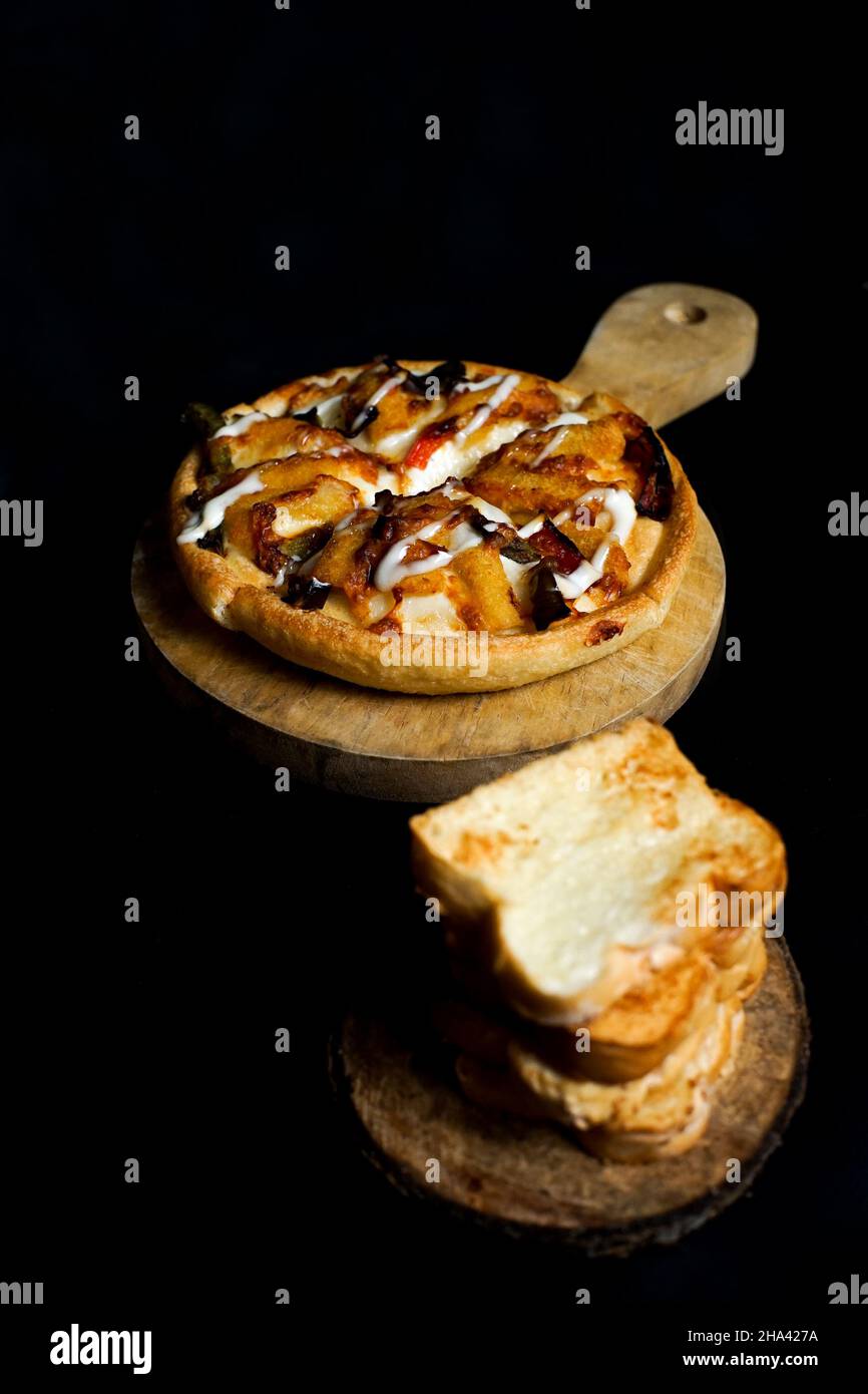 quatre tranches de pizza sur le paddle ou pelage en bois et une pile de pain blanc grillé. la nourriture occidentale isolée sur noir. Banque D'Images