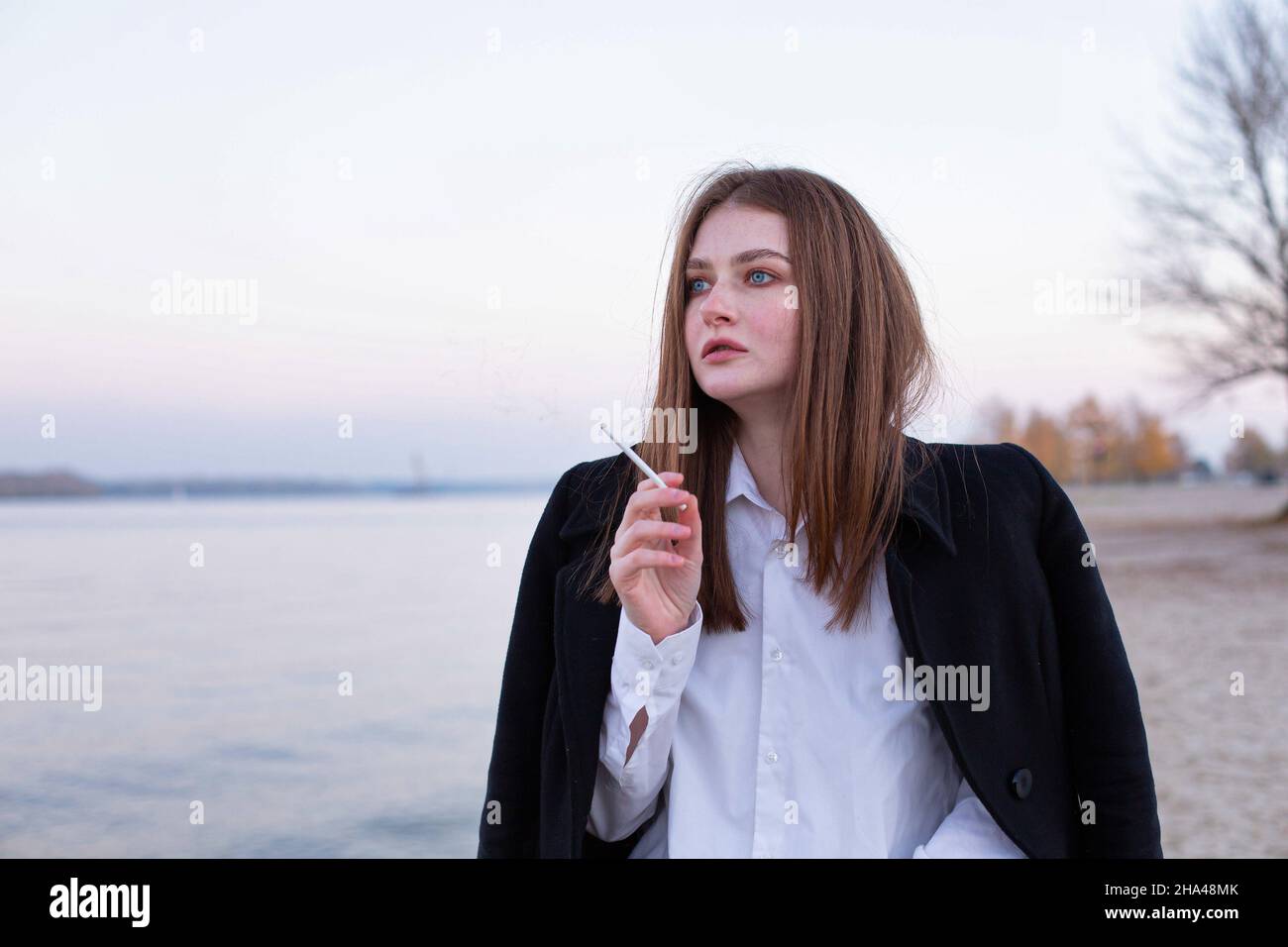 Femme européenne blanche fume, droite et longue, en manteau foncé en automne sur la plage Banque D'Images