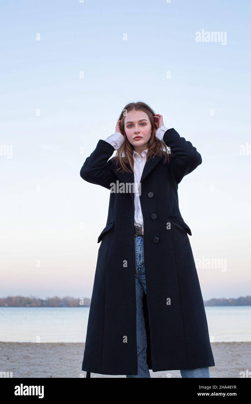 Femme européenne blanche à poils longs et droits en manteau foncé en automne sur la plage Banque D'Images