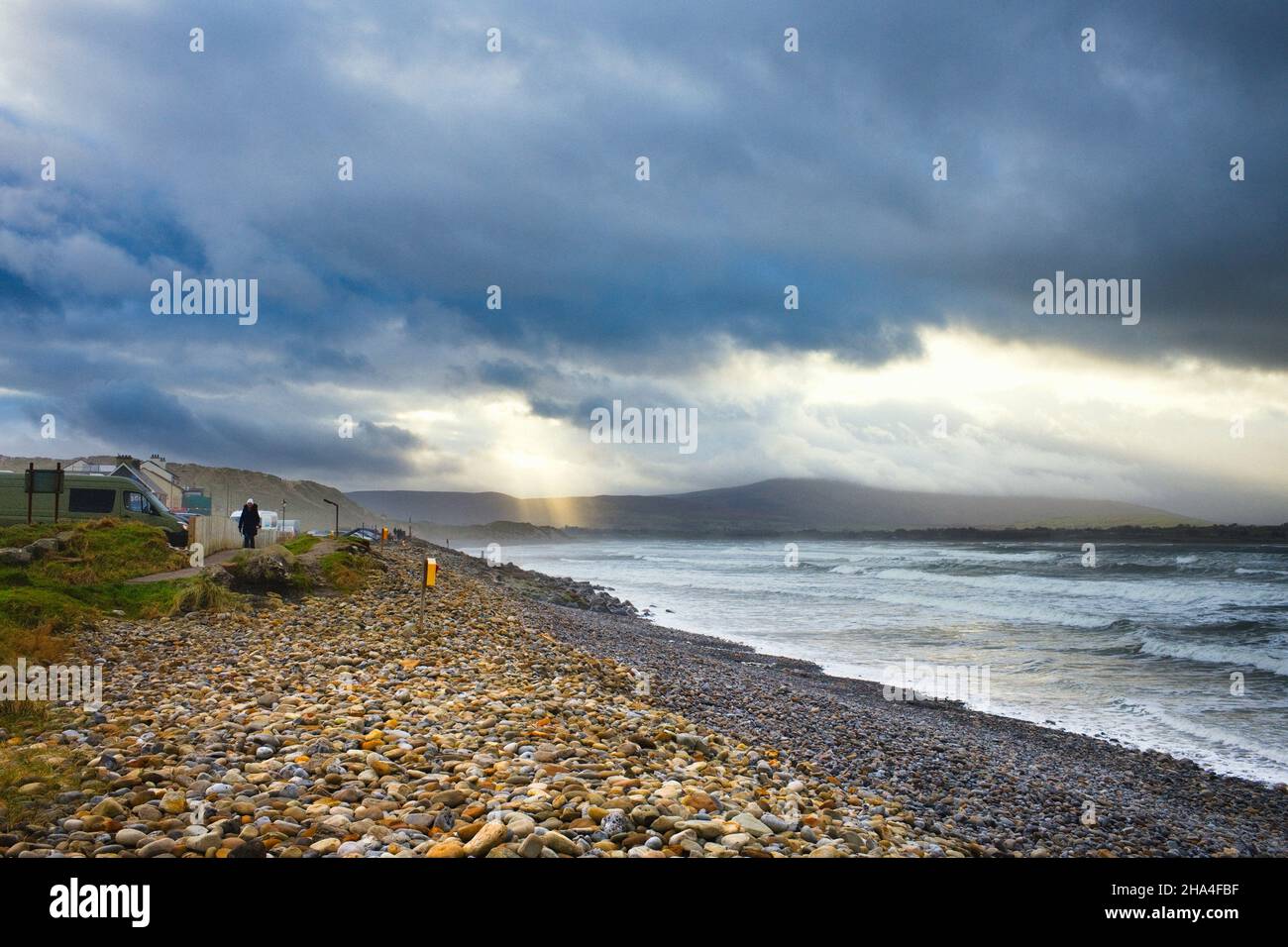 Femme seule marchant le long du chemin de la plage avec des mers orageux et des nuages sombres et un rayon de soleil à Strandhill, Sligo, Irlande Banque D'Images