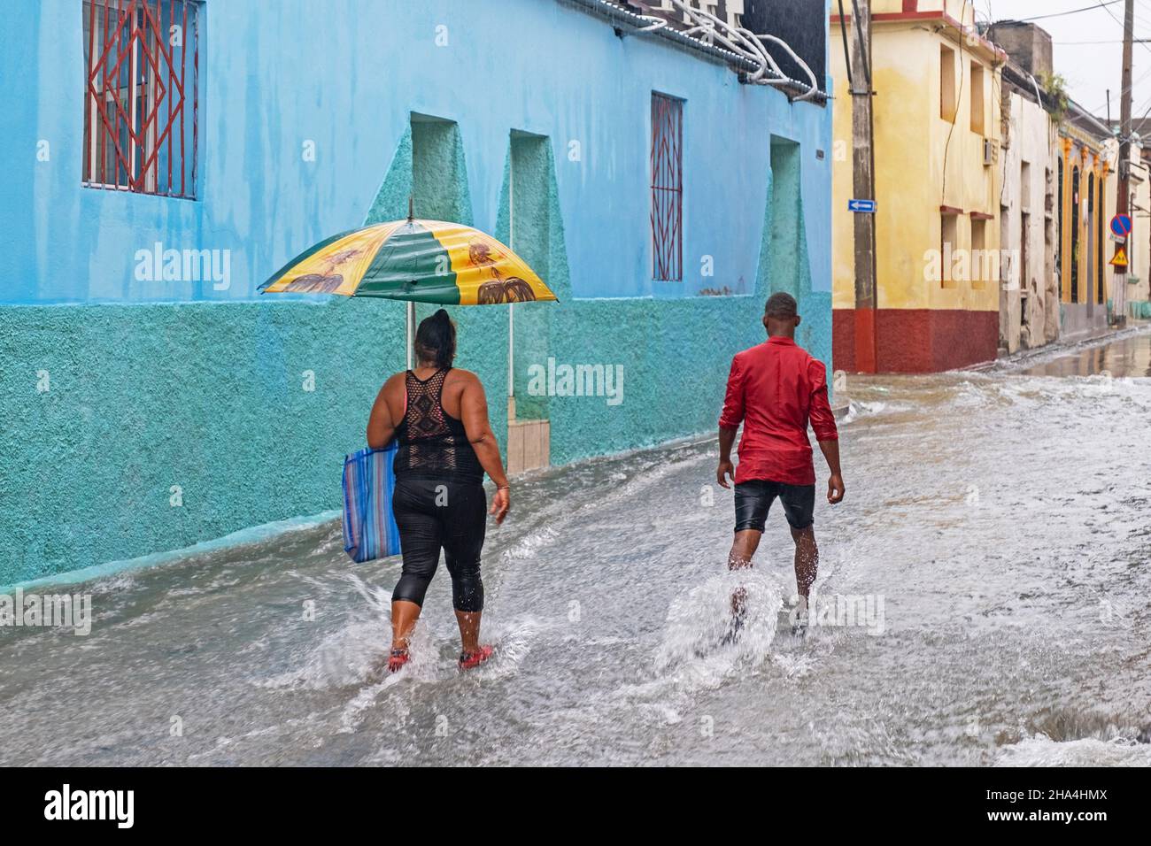 Cubains avec parasols marchant dans la rue inondée pendant la pluie torrentielle dans la ville de Santiago de Cuba sur l'île de Cuba, Caraïbes Banque D'Images
