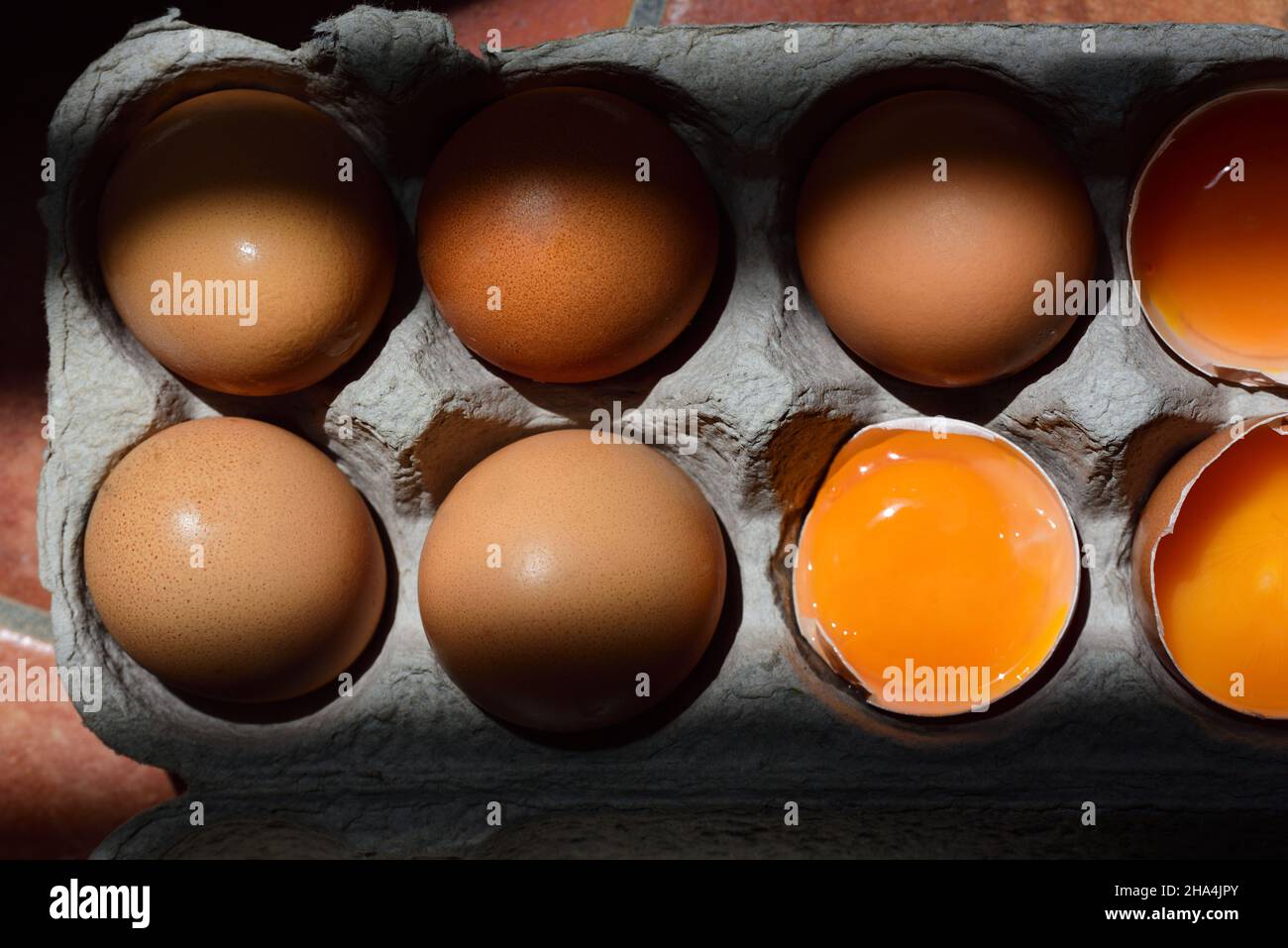 Dans une boîte à oeufs en carton sont plusieurs oeufs, dont certains sont encore intacts et d'autres ouverts avec le jaune d'oeuf, photographié d'en haut, dans une pièce o Banque D'Images