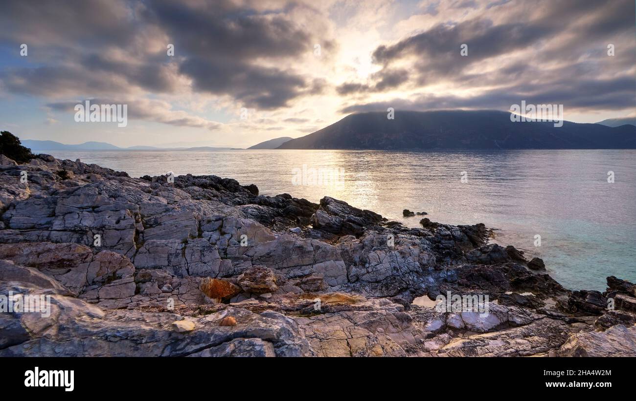 grèce,iles grecques,iles ioniennes,kefalonia,fiskardo,humeur du matin,ciel partiellement nuageux,image hdr,vue du lever de soleil derrière les nuages gris,roches colorées au premier plan,sunbeam sur la mer,ithaca sous les nuages Banque D'Images