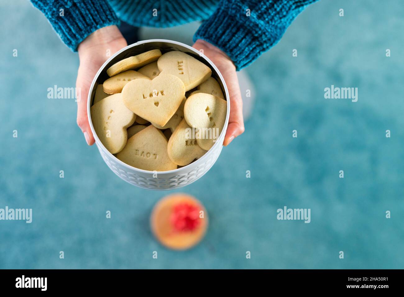 Saint Valentin.Mains de femme avec boîte à biscuits.Biscuits en forme de coeur et lettres D'AMOUR.Copier l'espace.Vue de dessus.Arrière-plan bleu. Banque D'Images