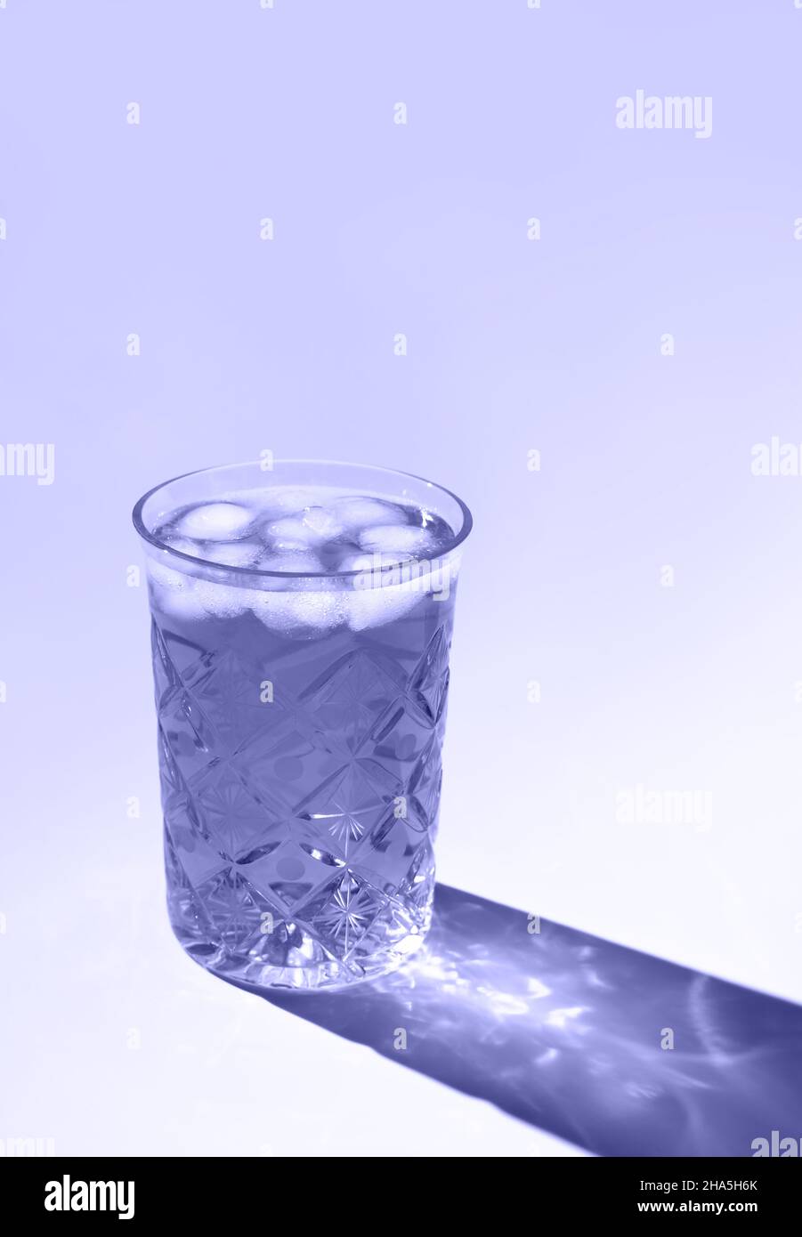 Le magnifique verre en cristal projette une ombre longue de la lumière du soleil.Coloris tendance de l'année 2022.Composition créative minimale avec espace de copie.Concept des boissons d'été. Banque D'Images