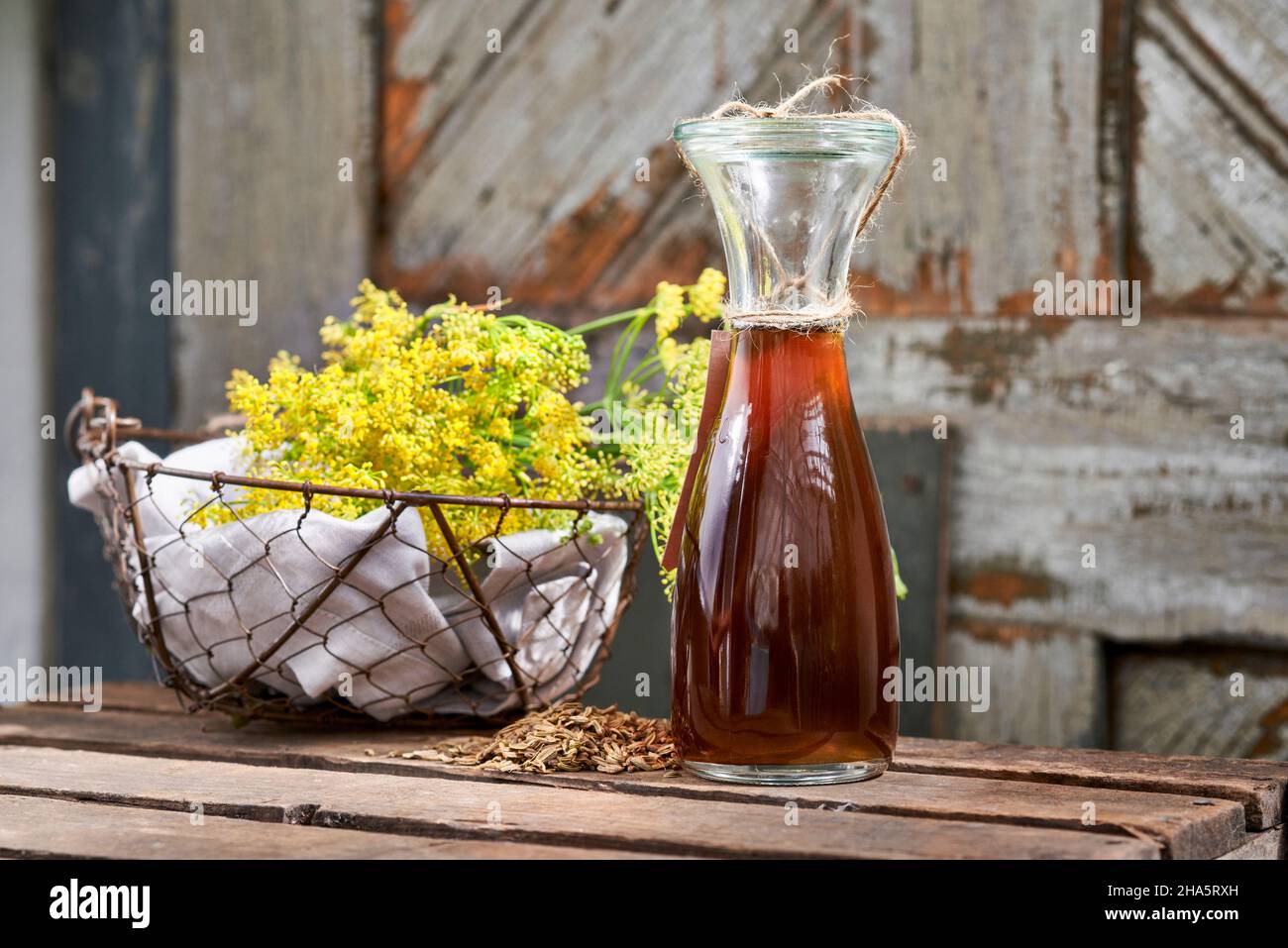 étapes de travail avec le fenouil et les graines de fenouil pour la préparation du sirop de fenouil, panier en fil avec fleurs de fenouil et bouteille de weck avec sirop de fenouil sur une table en bois devant une vieille porte en bois Banque D'Images