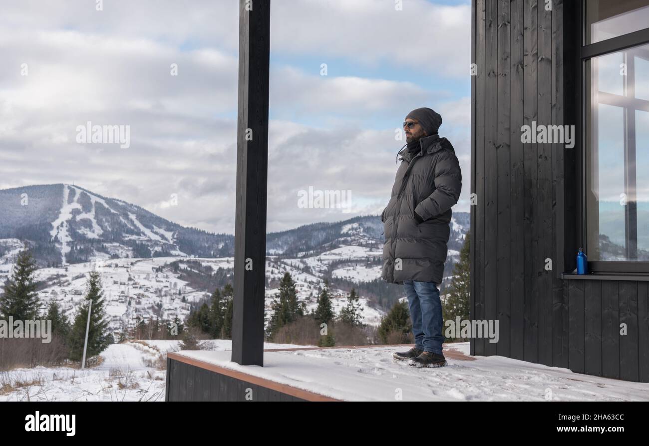 Homme debout sur la terrasse de la maison et regardant les montagnes enneigées Banque D'Images