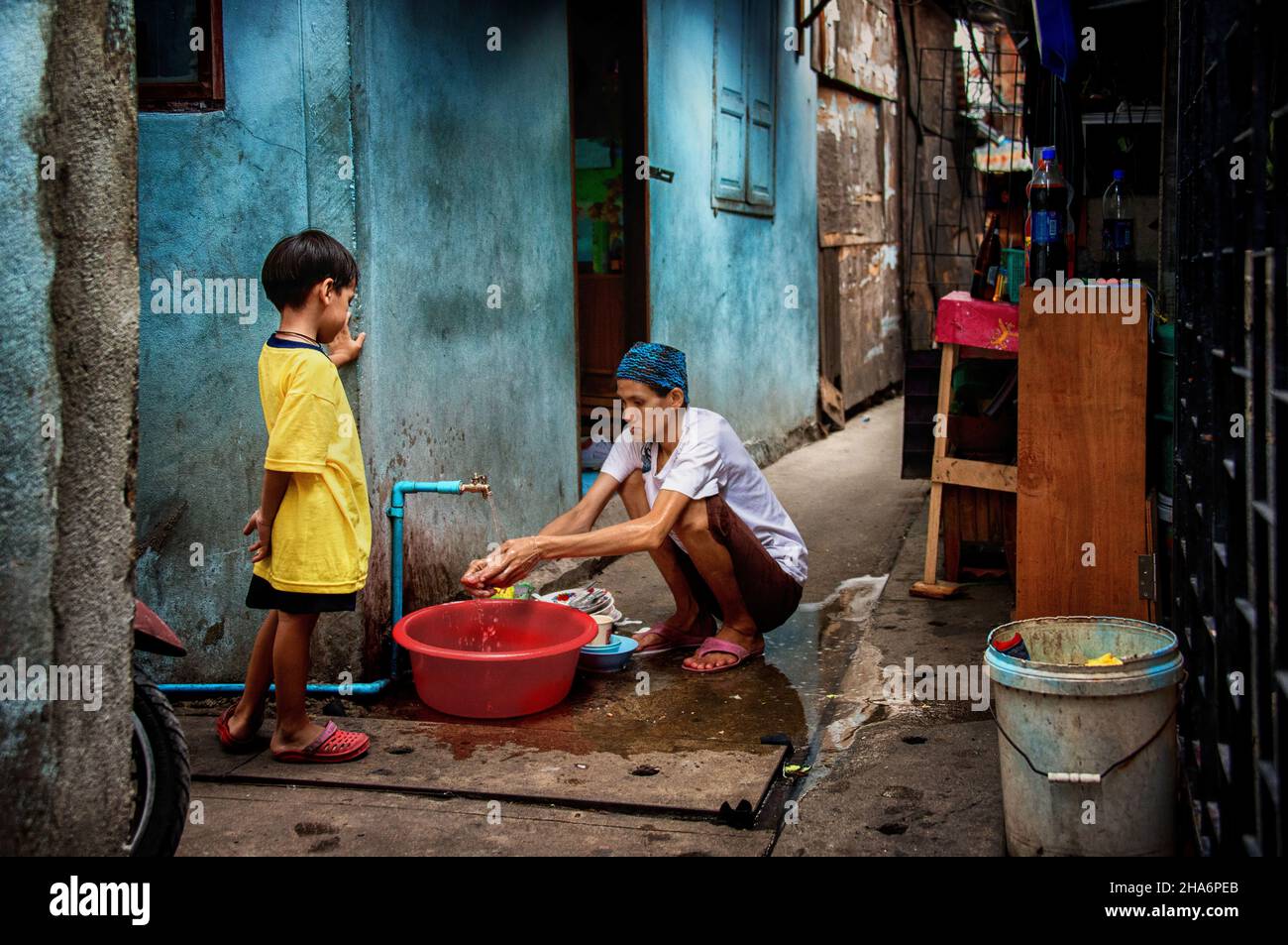 Une femme lave des plats pendant que son fils regarde dans le quartier Khlong Toei de Bangkok Thaïlande Banque D'Images
