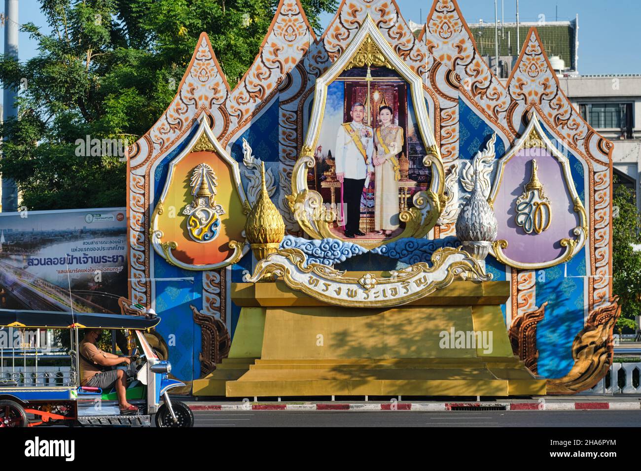 Un tuk-tuk (taxi à 3 roues) passe devant une grande décoration de rue avec le roi Maha Vajiralongkorn et la reine Suthida; Bangkok, Thaïlande Banque D'Images
