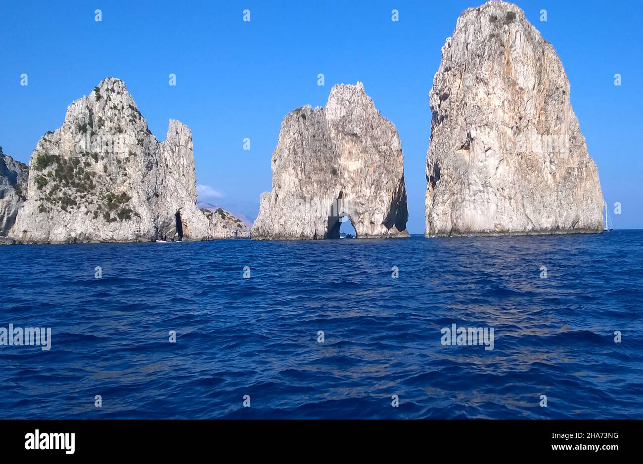La formation rocheuse connue sous le nom de Faraglioni de Mezzo, juste à côté de l'île de Capri, en Italie, sont considérées comme la vue la plus emblématique de l'île c'est une tradition qui embrasse un partenaire sous la petite arche lorsqu'un bateau passe à travers elle apporte de la chance au couple concerné. Banque D'Images