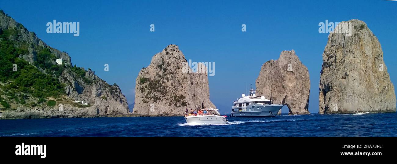 Les bateaux qui passent entre la formation rocheuse connue sous le nom de Faraglioni de Mezzo, juste à côté de l'île de Capri, en Italie, sont considérés comme la vue la plus emblématique de l'île c'est une tradition qui embrasse un partenaire sous l'arche lorsqu'un bateau passe à travers elle apporte de la chance au couple concerné.Le bateau dans le centre est le bateau à moteur de charter IDOL, Banque D'Images