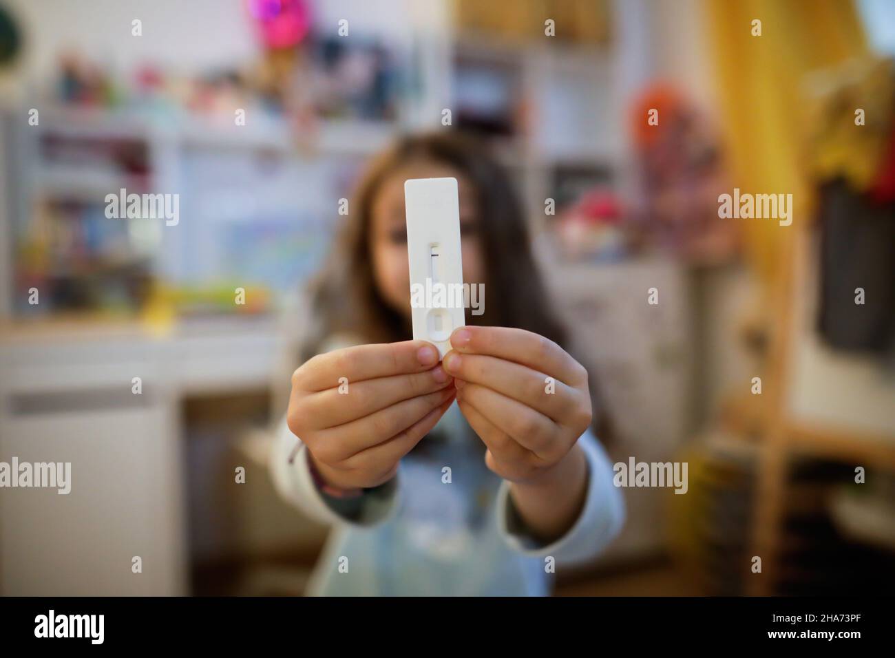 Détails de faible profondeur de champ (foyer sélectif) avec les mains d'une fille de 6 ans tenant un test rapide d'antigène COVID-19, avec un résultat négatif. Banque D'Images