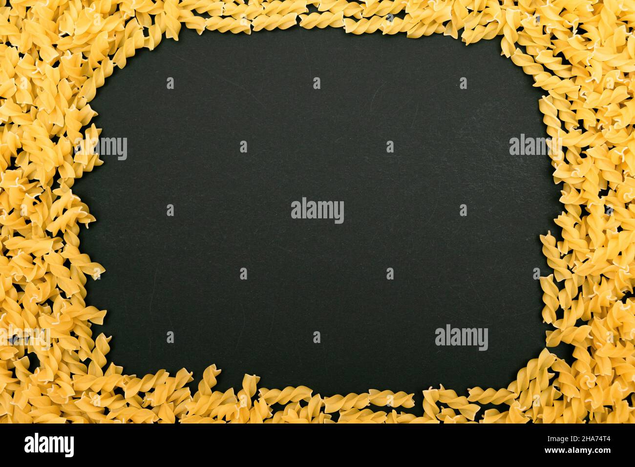 Un cadre fait de pâtes Fusilli non cuites éparpillées sur une table noire - maquette.Macaroni cru et sec.Aliments malsains et gras.Culture italienne Banque D'Images