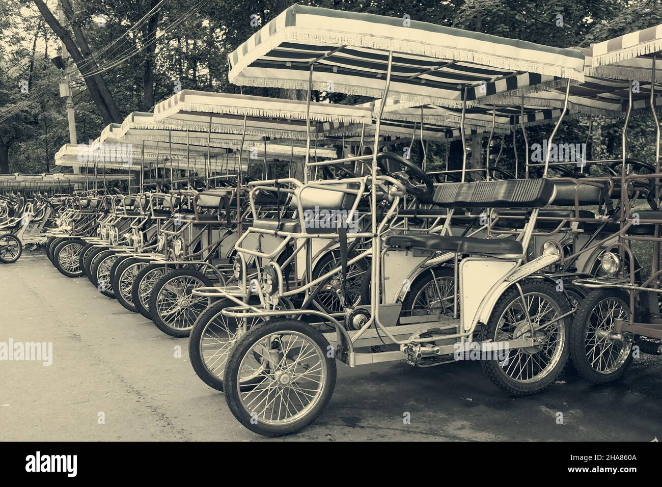 Une rangée de vélos d'époque à pédales et à quatre roues à louer sur le stationnement dans un parc public.Location de quad rétro dans sépia ton. Banque D'Images