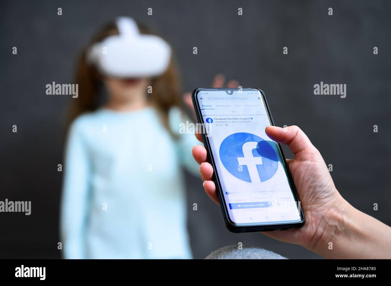 Moscou - 2 décembre 2021: Personne regarde les médias sociaux Facebook dans le téléphone mobile sur le fond de l'enfant à l'aide d'un casque futuriste de réalité virtuelle.Concept de Banque D'Images