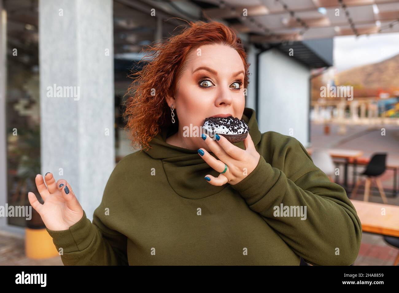 Portrait d'une femme bien nourrie surprise mangeant un donut de chocolat choquant.Le concept de régime alimentaire et d'obésité. Banque D'Images