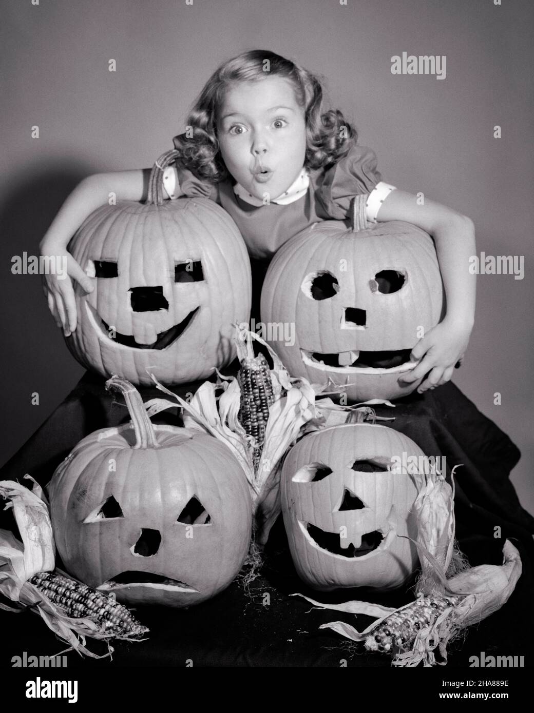 1950S PETITE FILLE DEBOUT AU-DESSUS DE QUATRE CITROUILLES D'HALLOWEEN SCULPTÉES JACK-O-LANTERNES AVEC L'EXPRESSION FACIALE EFFRAYÉE REGARDANT LA CAMÉRA - H2948 DEB001HARS STUDIO SHOT HOME VIE COPIE ESPACE HUG SYMBOLES PEUR EXPRESSIONS B&W CONTACT OCULAIRE ANXIÉTÉ TÊTE ET ÉPAULES CITROUILLES ANXIEUXEXCITATION SCULPTÉE CONCEPT CONCEPTUEL MENACÉ CRAINTIF MALAISE DEB001 JACK-O-LANTERNES OCTOBRE CONCEPTS SYMBOLIQUES JUVÉNILES OCTOBRE 31 BLANC ET NOIR AUTOMNAL CAUCASIENREPRÉSENTATION ETHNIQUE À L'ANCIENNE Banque D'Images