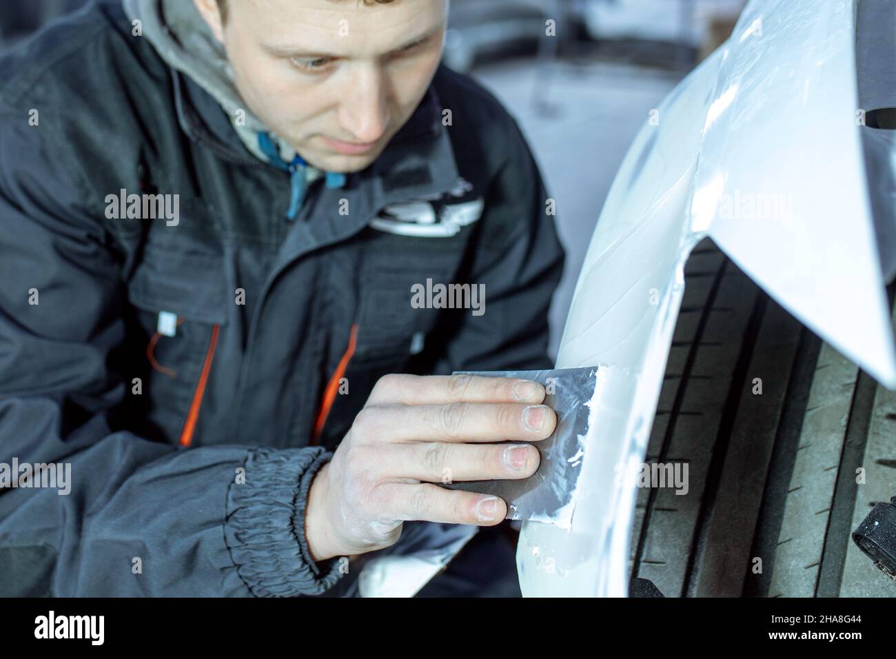 Réparation de la carrosserie de voiture par le ficelage de gros travaux après l'accident en travaillant le primaire de ponçage avant la peinture., le mécanicien répare la voiture , en utilisant Banque D'Images