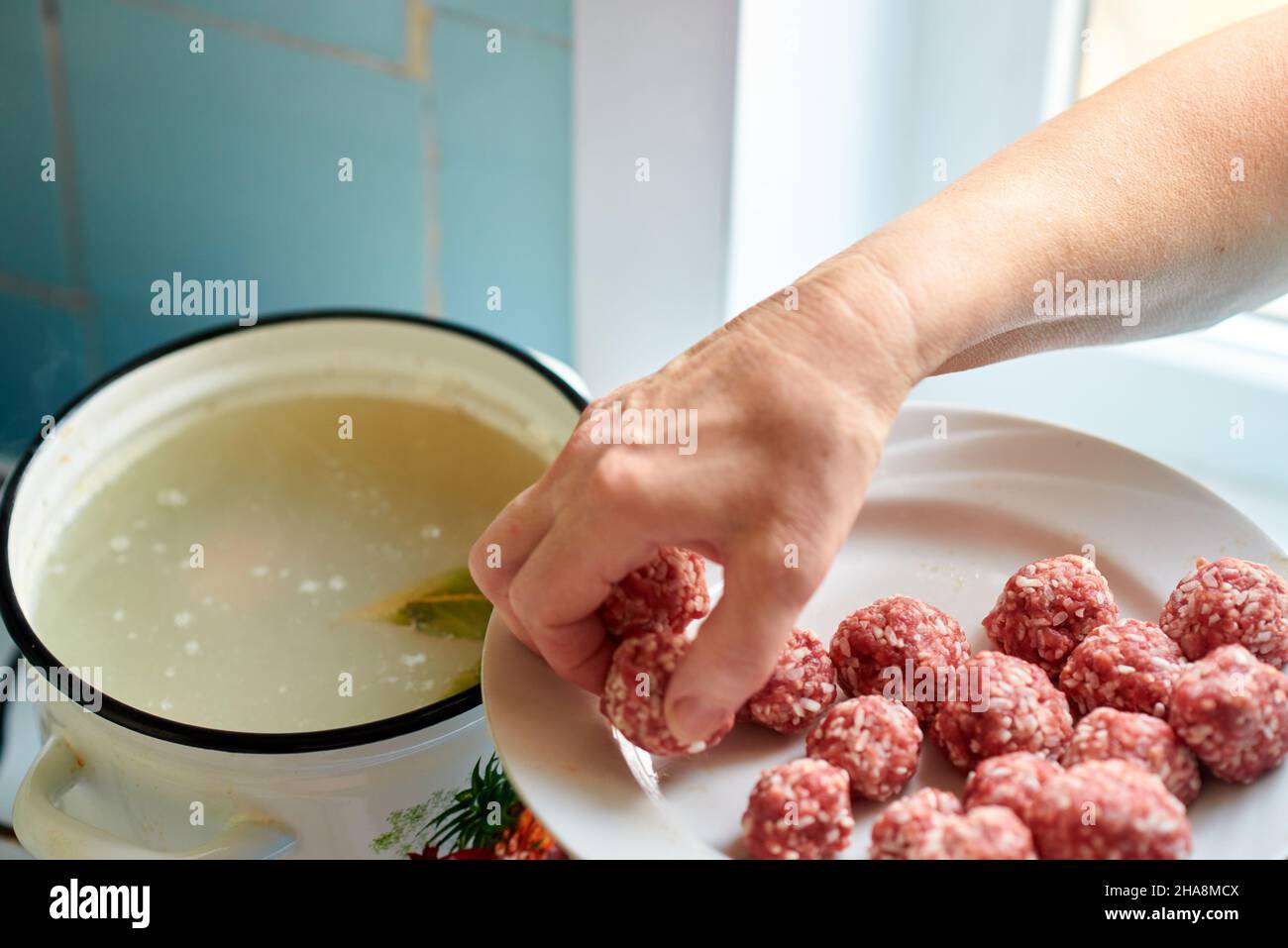 La main d'une femme prend des boulettes de viande crues d'une assiette et les jette dans un pot de soupe bouillante.Une cuisine maison saine. Banque D'Images