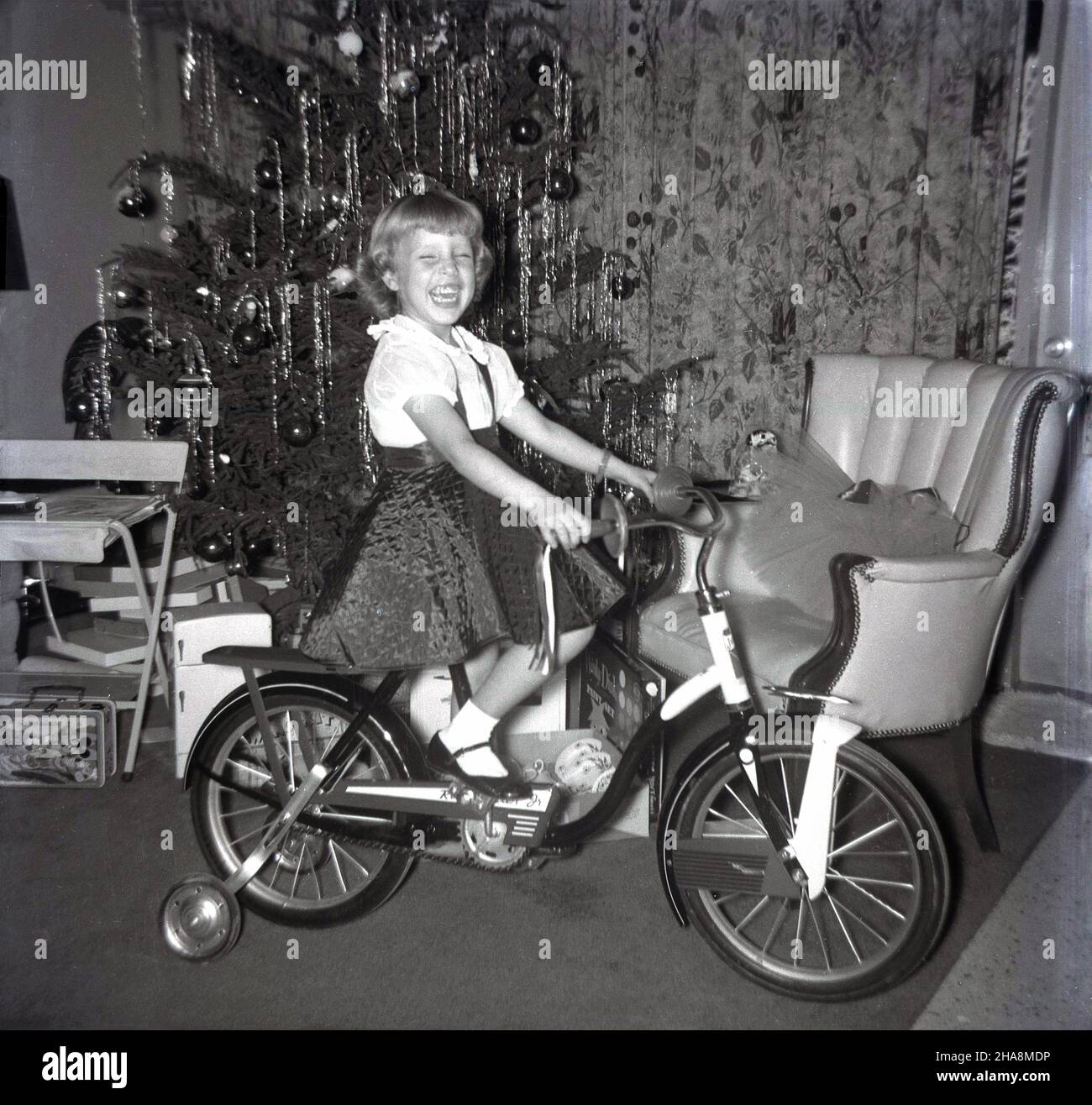 1960s. historique, une jeune fille excitée et ravie assis sur son cadeau de noël, une nouvelle bicyclette. Banque D'Images
