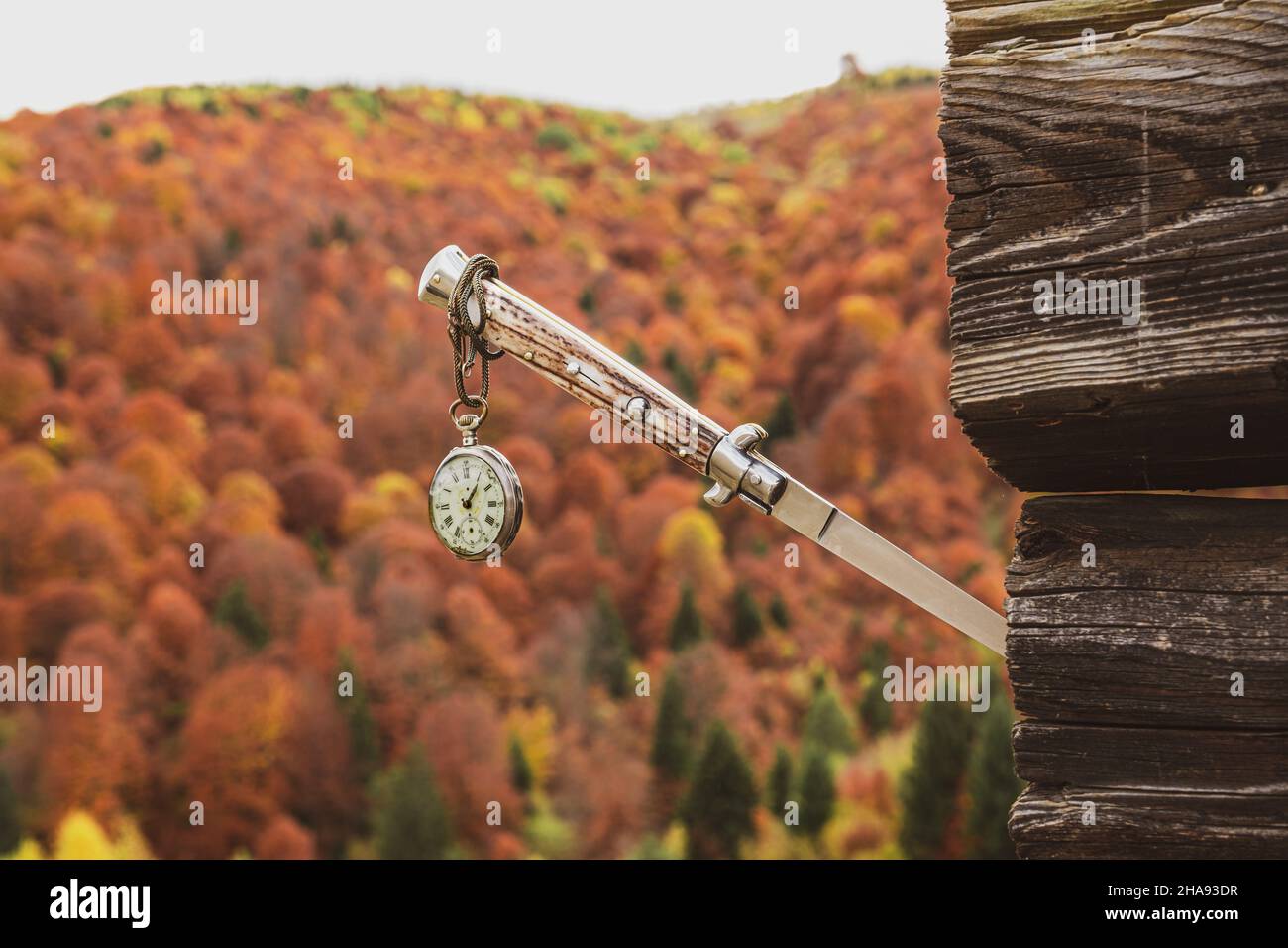une vieille montre accrochée à un couteau coincé dans un vieux cottage avec un paysage d'automne en arrière-plan Banque D'Images
