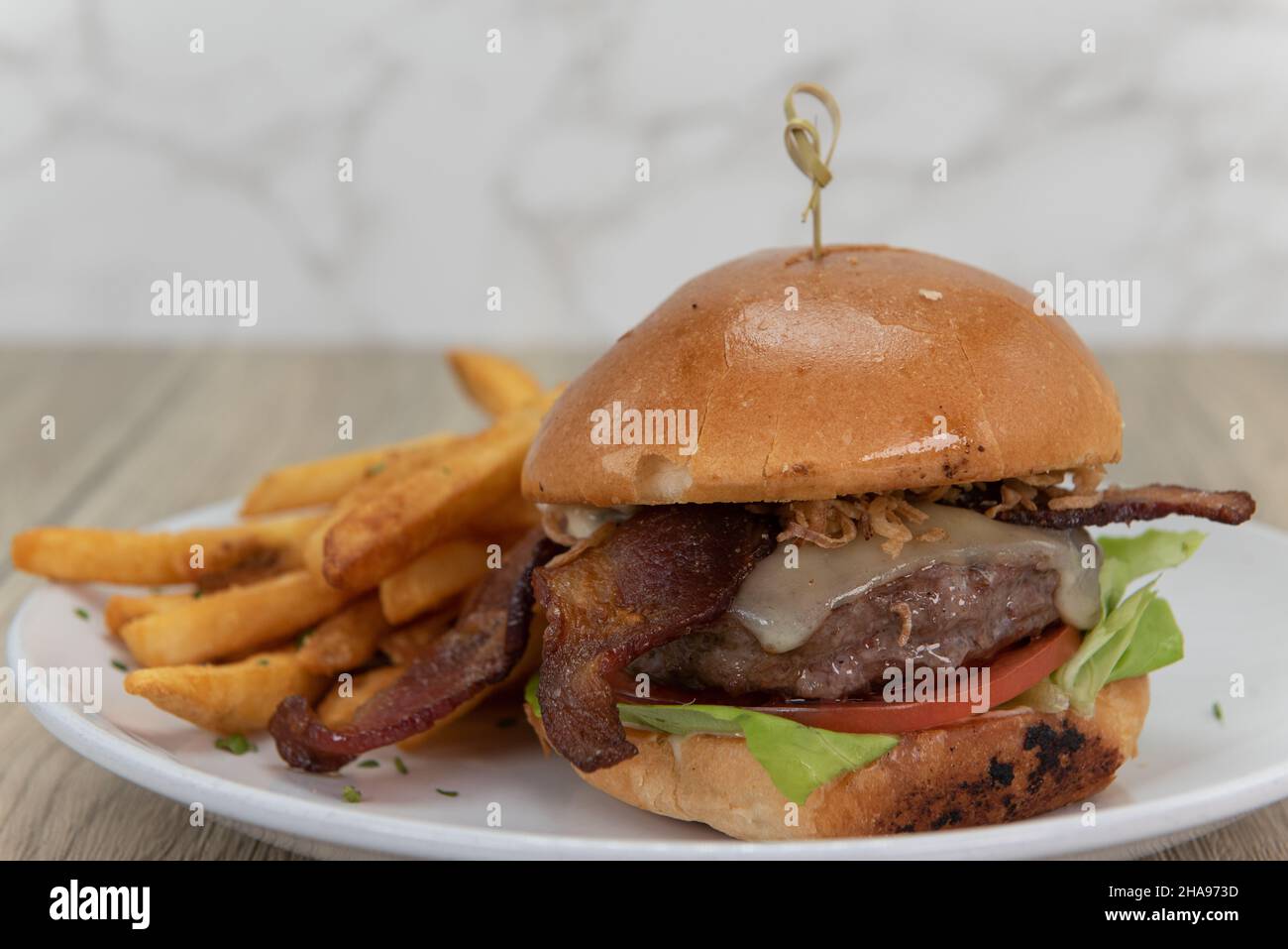 Présentation artistique du fromage fondu et du hamburger au bacon sur un pain beurré servi avec des frites croquantes. Banque D'Images