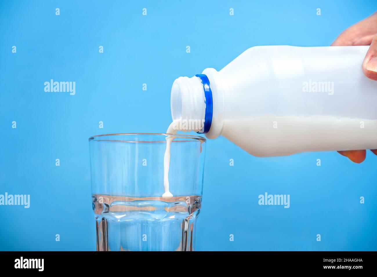 La femme verse du lait dans le verre à partir du biberon sur fond bleu Banque D'Images