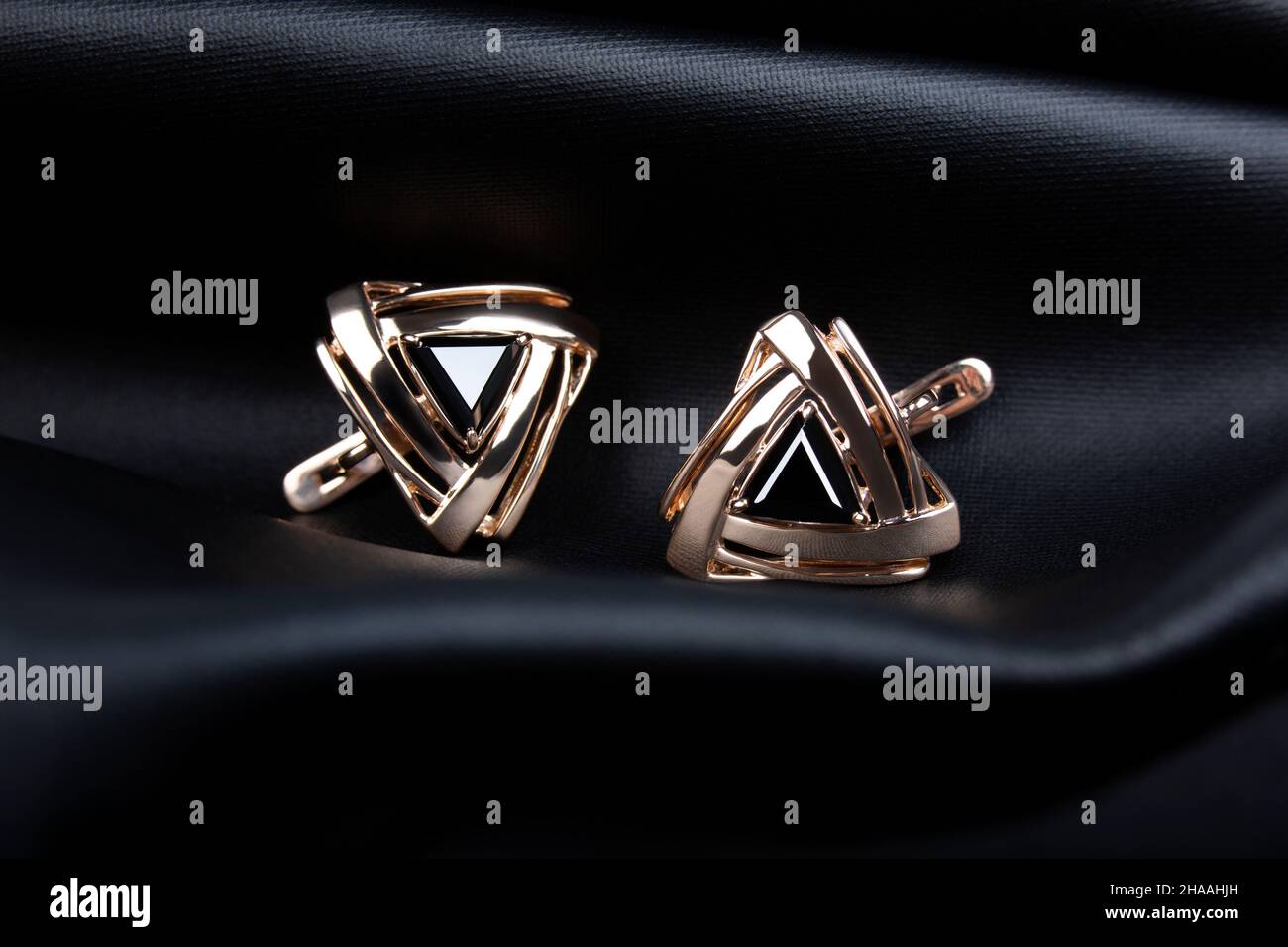 Boucles d'oreilles dorées avec pierre noire sur fond en cuir noir Banque D'Images