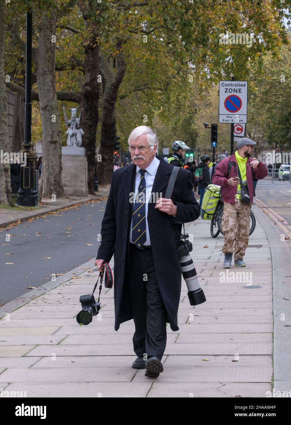 Un photographe âgé, bien habillé avec plusieurs appareils photo, descend dans la rue à Victoria Embankment avant le Lord Mayor Show 2021. Banque D'Images