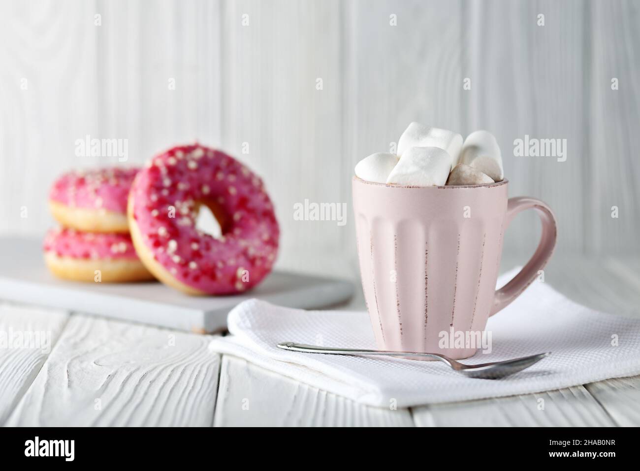 Beignets à la verglaçure rose et en poudre de caramel de couleur et cacao avec guimauves sur fond de bois blanc. Banque D'Images