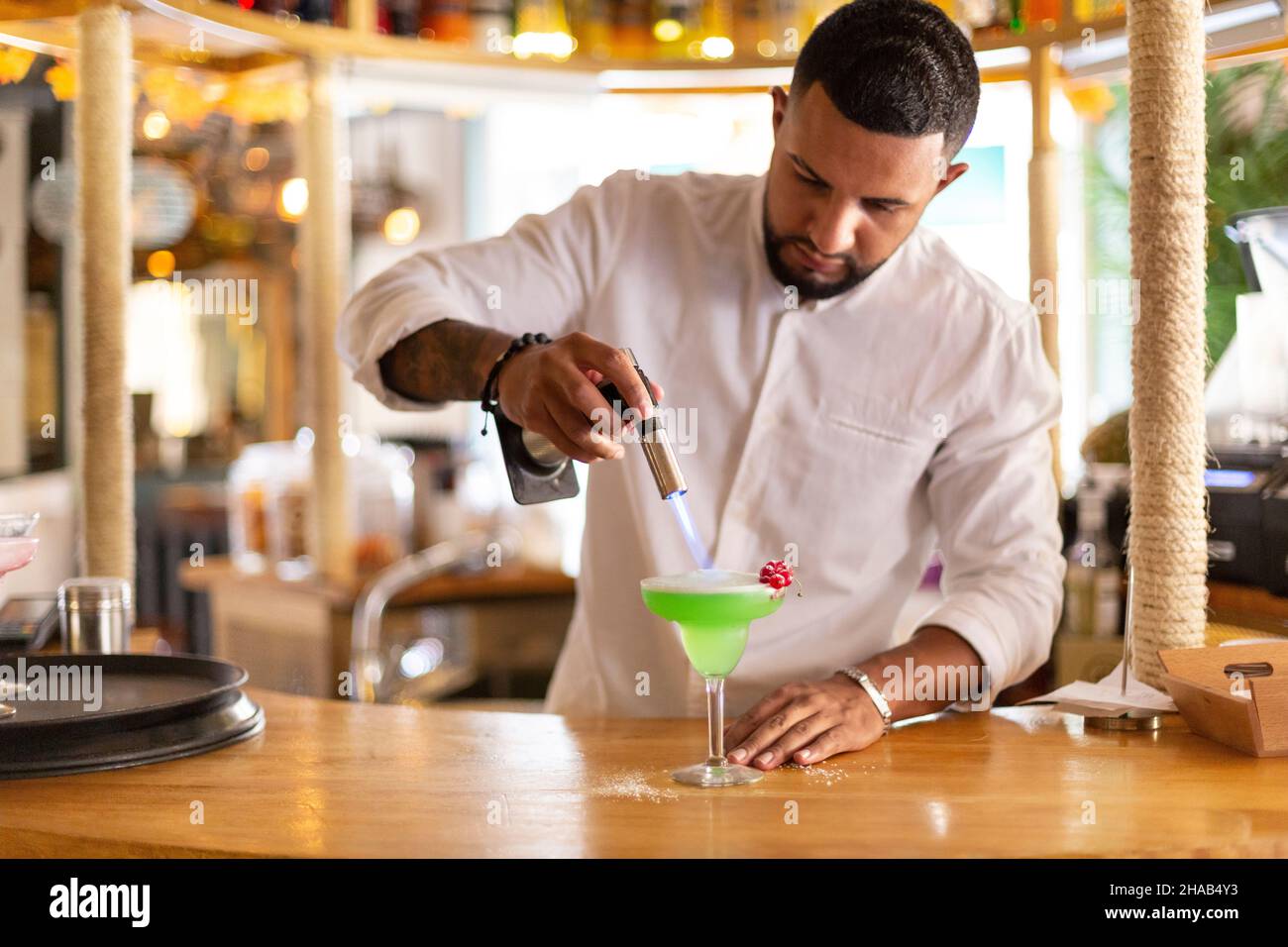 Un élégant jeune serveur latino-américain prépare avec soin une boisson alcoolisée dans un restaurant moderne.Espace pour le texte.Mise au point sélective. Banque D'Images