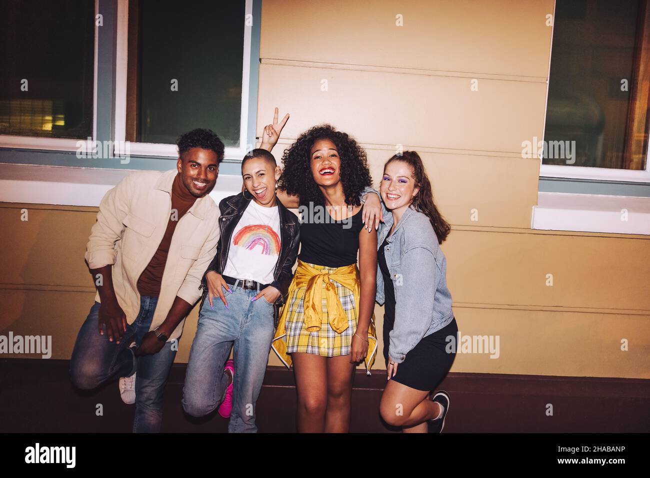 Des amis heureux se penchent contre un mur la nuit.Groupe de jeunes multiculturels souriant à la caméra tout en se tenant ensemble à l'extérieur.Joyeux fr Banque D'Images