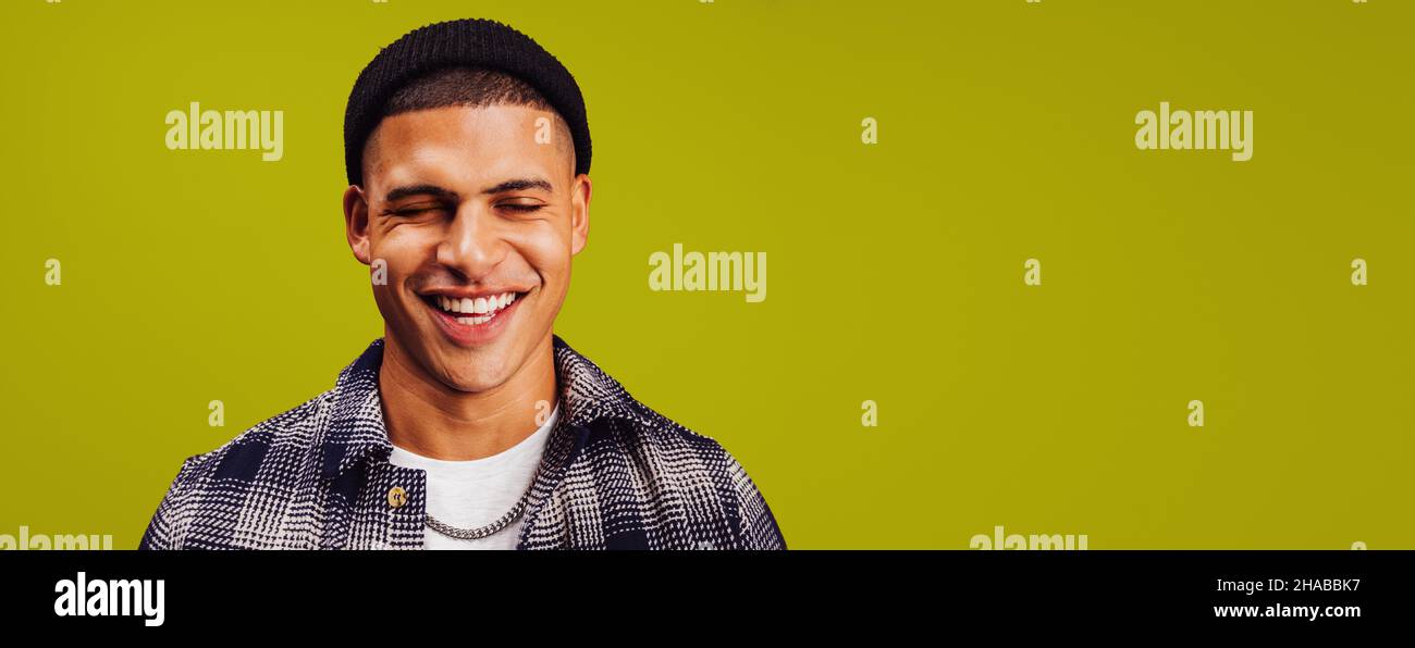 Beau jeune homme souriant avec ses yeux fermés dans un studio.Un jeune homme heureux portant un bonnet noir sur fond de studio.Jeune homme recherche che Banque D'Images