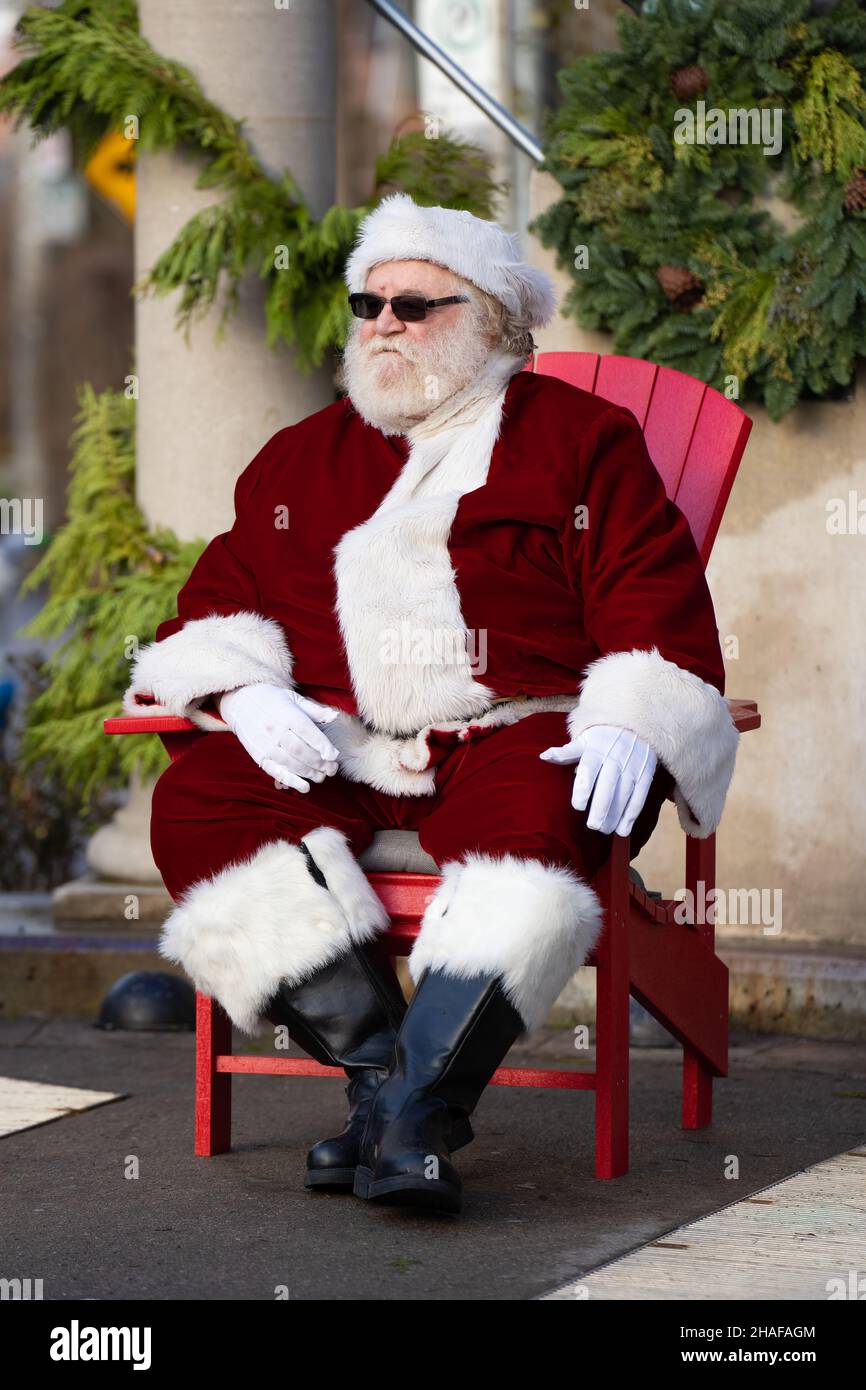 Un père Noël super cool redonne un coup de pied dans une chaise Muskoka lors d'un événement de Noël dans le quartier de Greektown à Toronto. Banque D'Images