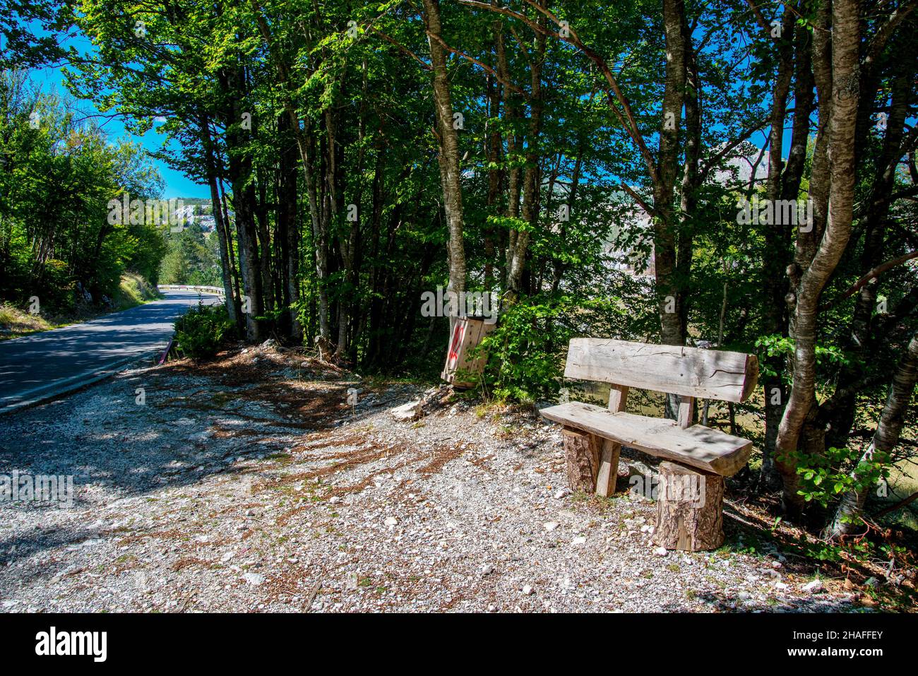 En septembre, un siège fait de grumes d'arbre, pour les randonneurs fatigués de se reposer, à côté de l'étroite route de montagne bordée d'arbres, obscurcissant partiellement le Mont Lovcen b Banque D'Images