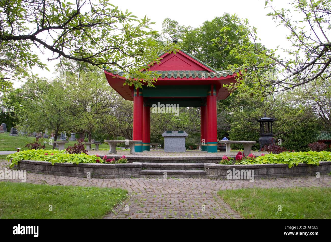 Petit temple rouge asiatique oriental avec fleurs dans le cimetière horizontal Banque D'Images