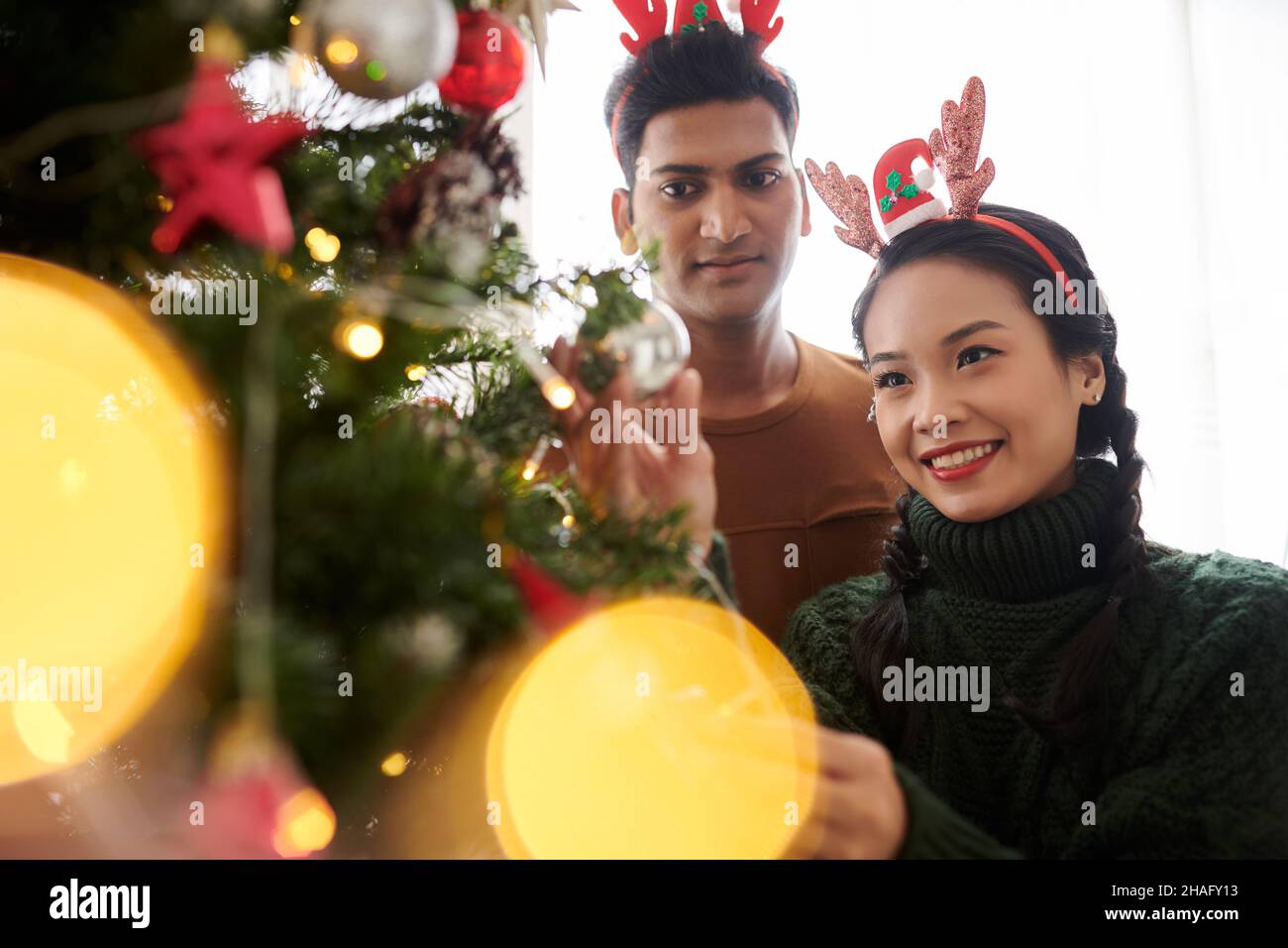 Joyeux jeune couple divers décorant l'arbre de Noël pour la célébration Banque D'Images