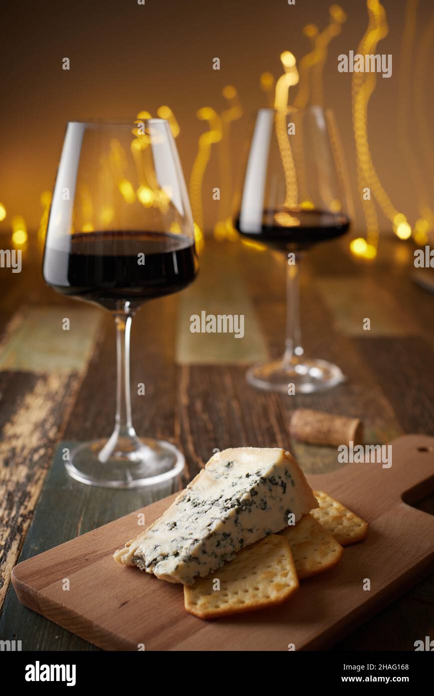 La vie de deux verres de vin, du fromage à la moisissure bleue et des craquelins sur une planche de bois sur le fond d'une guirlande du nouvel an.Vue avant. Banque D'Images