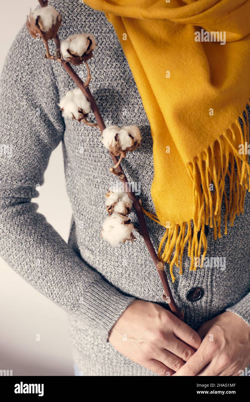 Un homme dans un gilet gris et une écharpe brillante est debout avec une branche de coton sur un fond clair.Vue avant. Banque D'Images