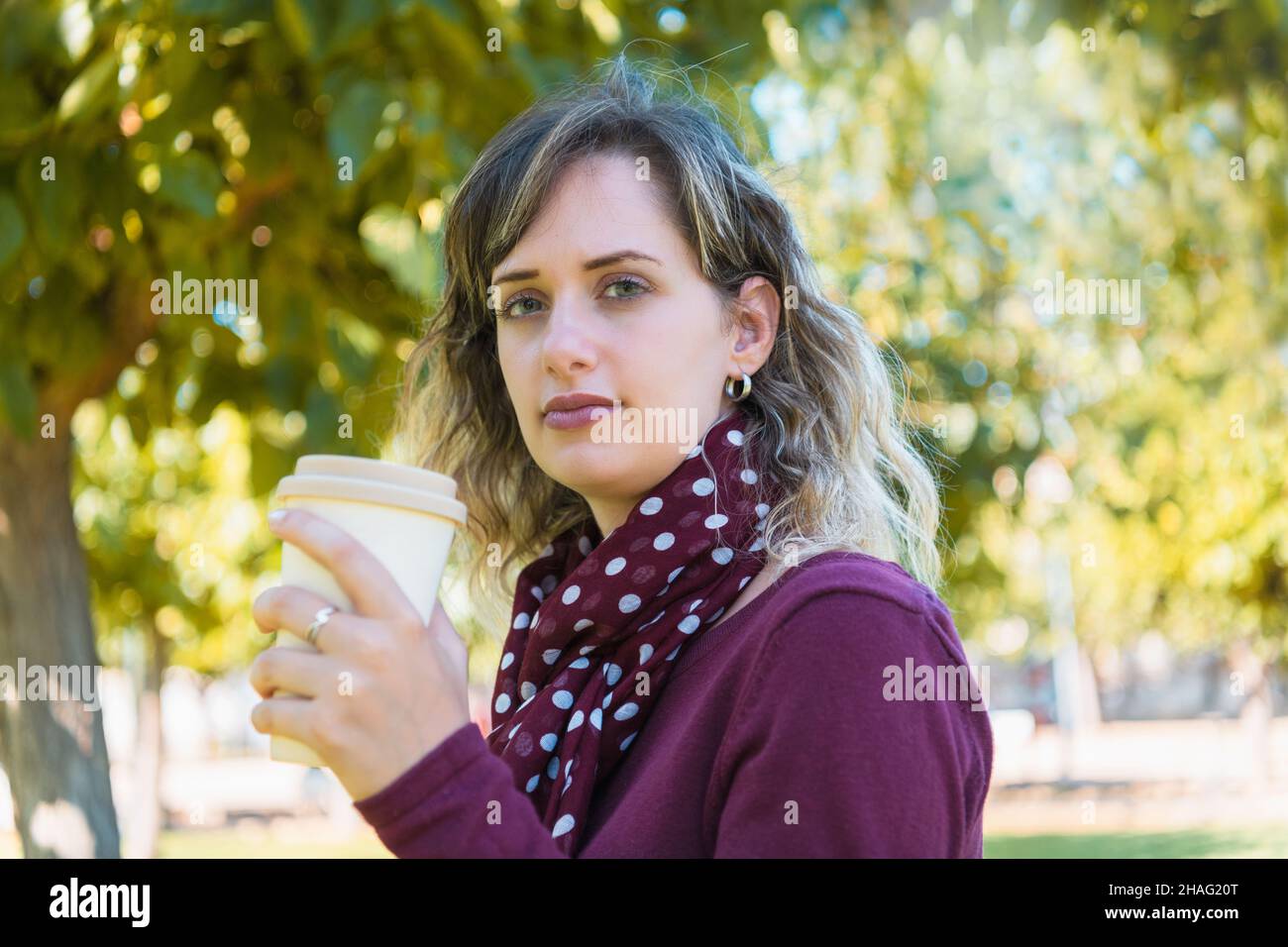 Femme blonde tenant un café à emporter dans un parc Banque D'Images