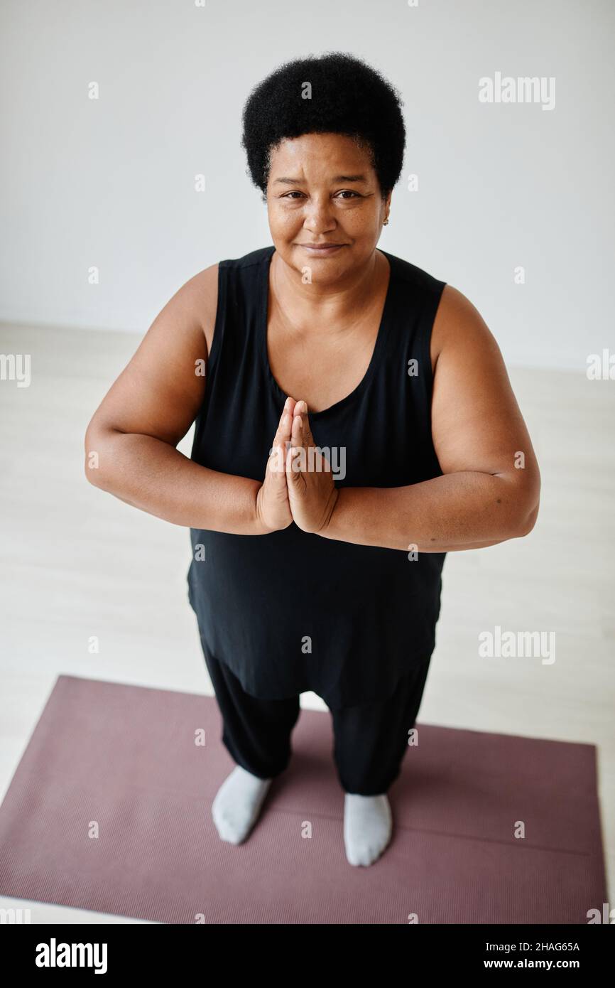 Portrait vertical en grand angle d'une femme âgée noire appréciant le yoga à l'intérieur et souriant à l'appareil photo Banque D'Images