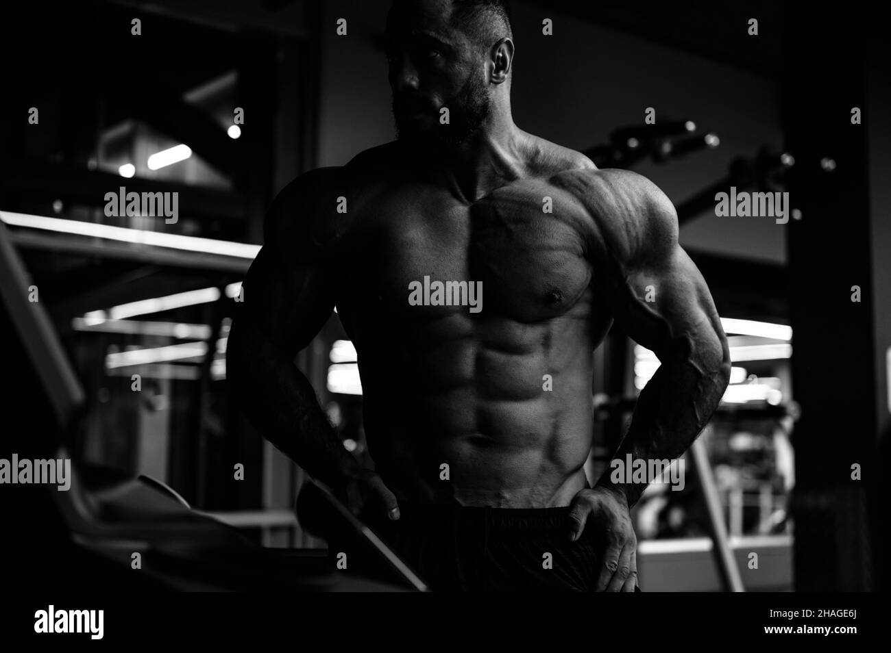 jeune athlète fort avec la barbe montrant son corps musculaire puissant dans le sport de nuit fitness gym Banque D'Images