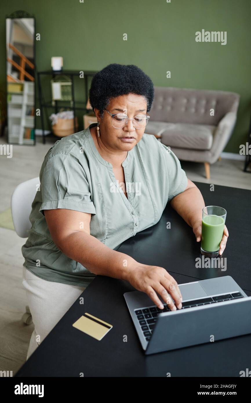 Portrait vertical d'une femme âgée noire utilisant un ordinateur portable à la maison et magasiner en ligne ou payer des impôts Banque D'Images