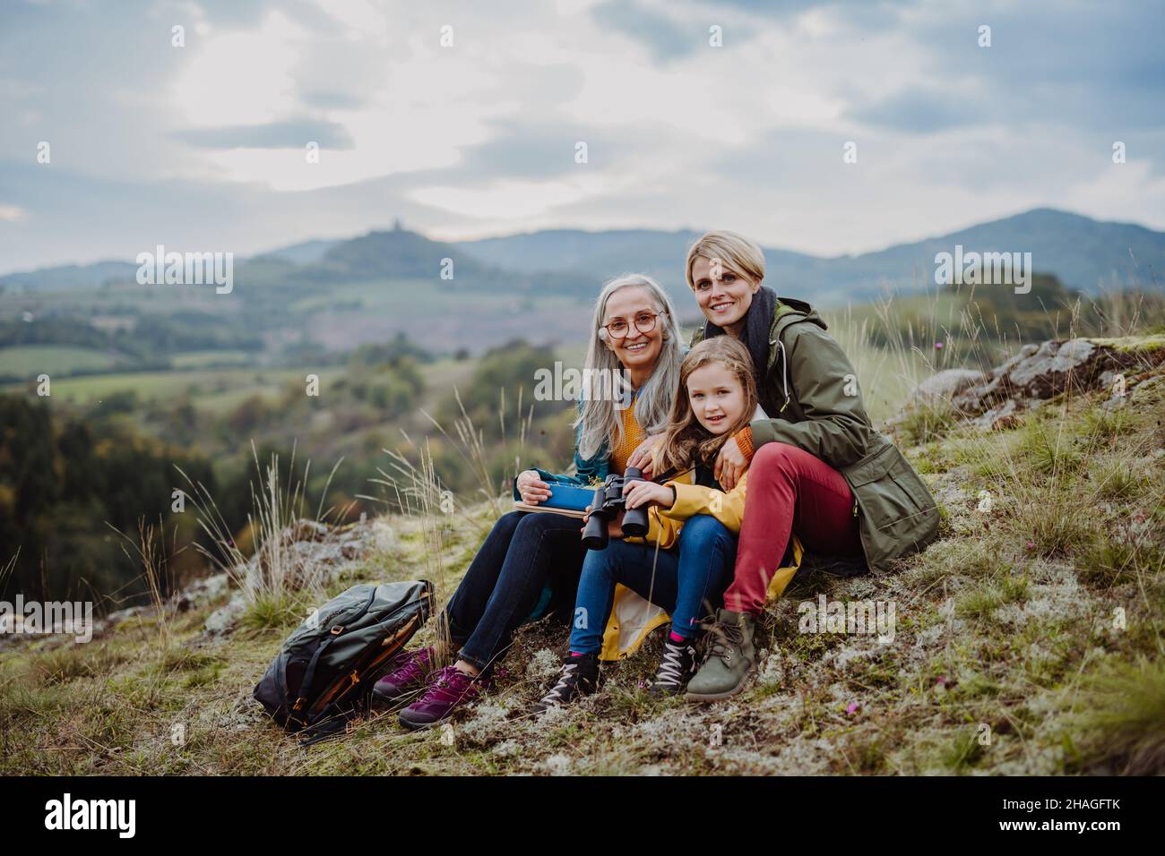 Petite fille avec mère et grand-mère assis et lookiong à la caméra sur le sommet de la montagne. Banque D'Images