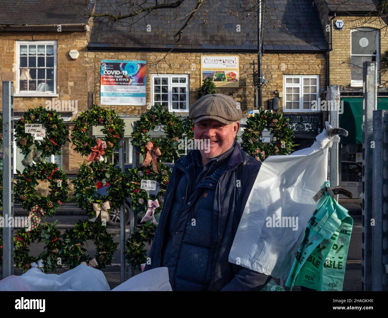 Marché souriant commerçant vendant une variété de plantes de Noël, y compris des couronnes, marché d'Olney, Buckinghamshire, Royaume-Uni Banque D'Images